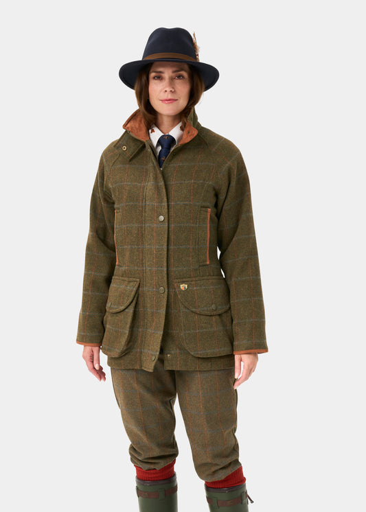 Woman in a Combrook Tweed Waterproof Shooting Coat (Willow) stands against a plain white background.