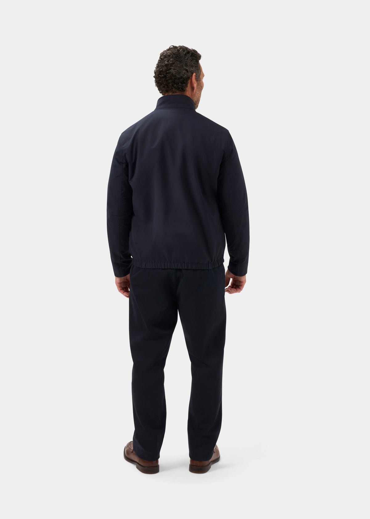 A man faces away in the Lakeward Men’s Reversible Bomber Jacket in navy and beige, with matching pants and brown shoes.