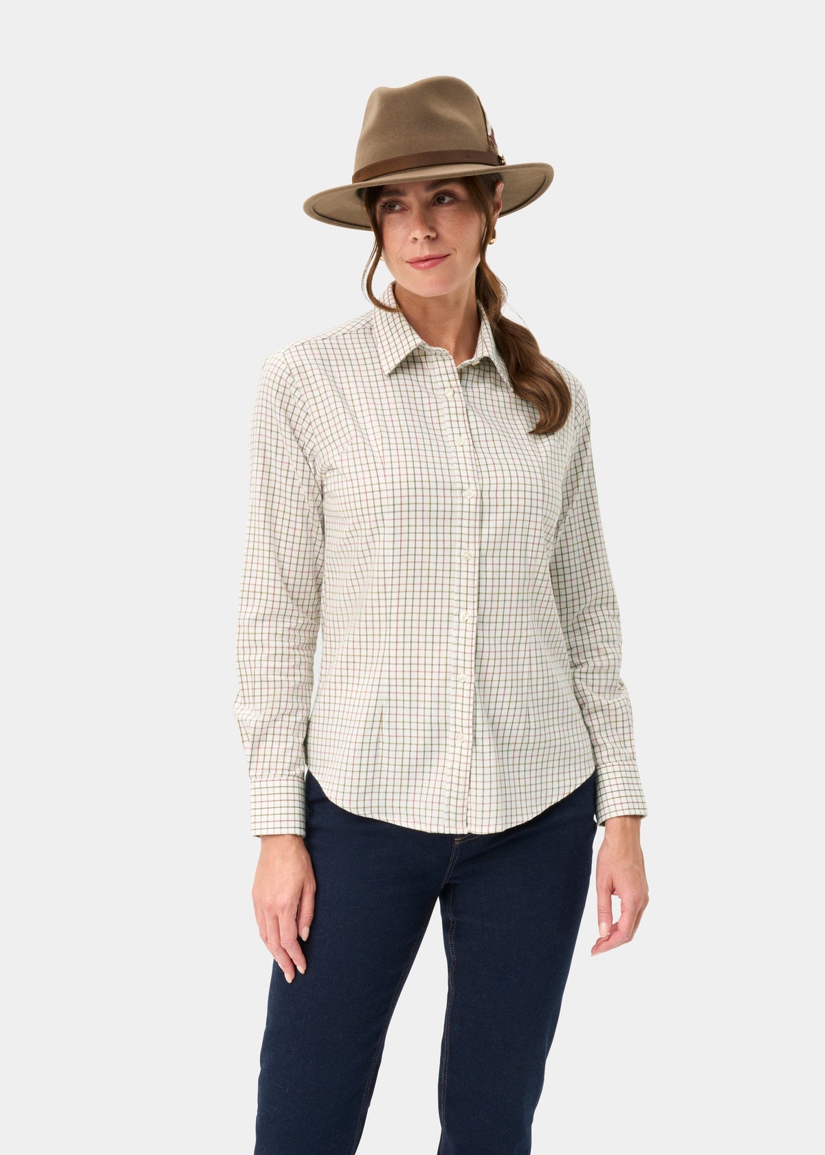 Woman in a Bromford Ladies Cotton Shirt in Olive Check, dark jeans, and brown hat stands against a white background.