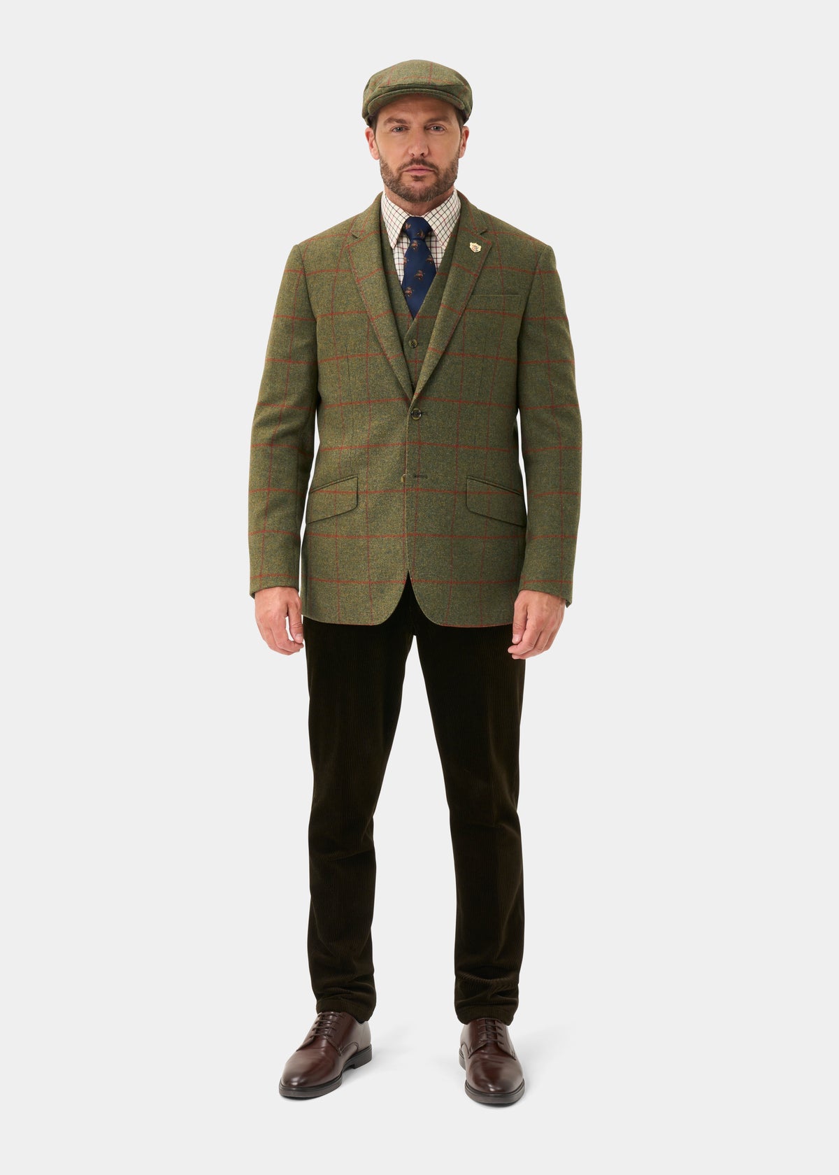 Man wears Combrook Men’s Tweed Water Repellent Sports Blazer in Reed, flat cap, tie, and dark pants on white backdrop.