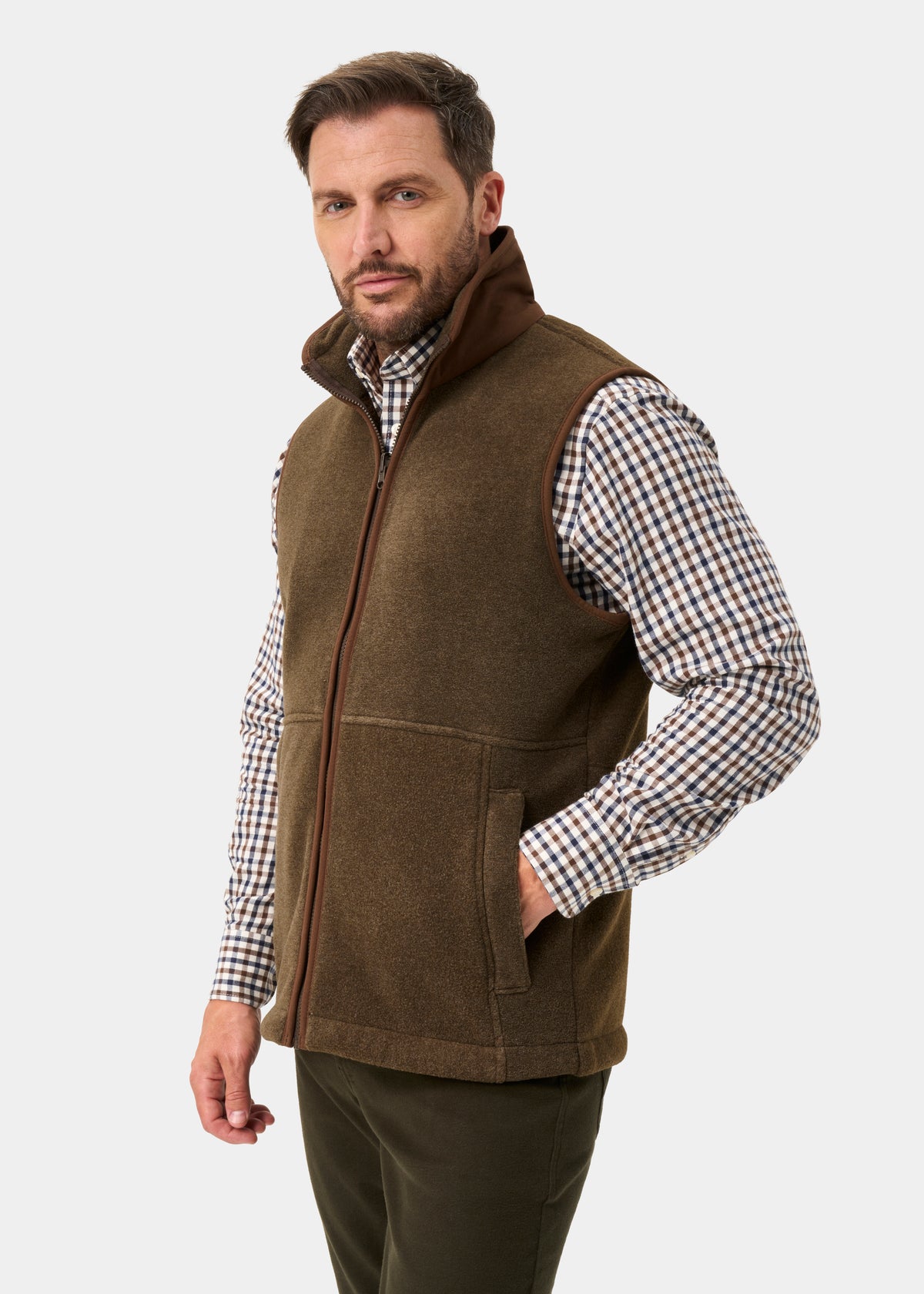 Man in Aylsham Men’s Fleece Gilet in Pecan, regular fit, over checkered shirt, hand in pocket, plain background.