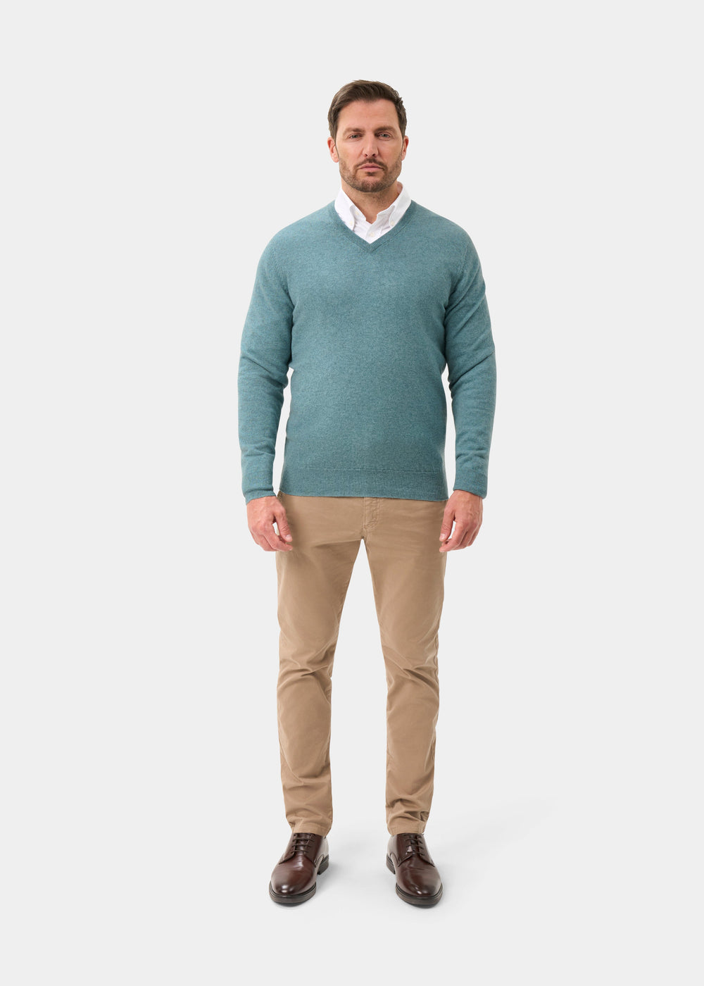 Man wearing Haddington Pure Cashmere V-Neck Jumper in Caspian, white shirt, khaki pants, and brown shoes.
