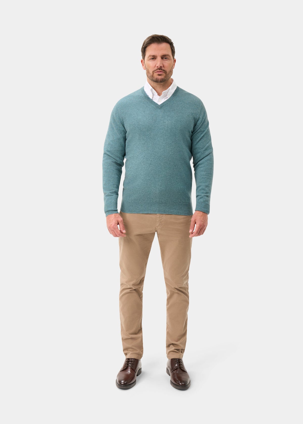 Man wearing Haddington Pure Cashmere V-Neck Jumper in Caspian, white shirt, khaki pants, and brown shoes.