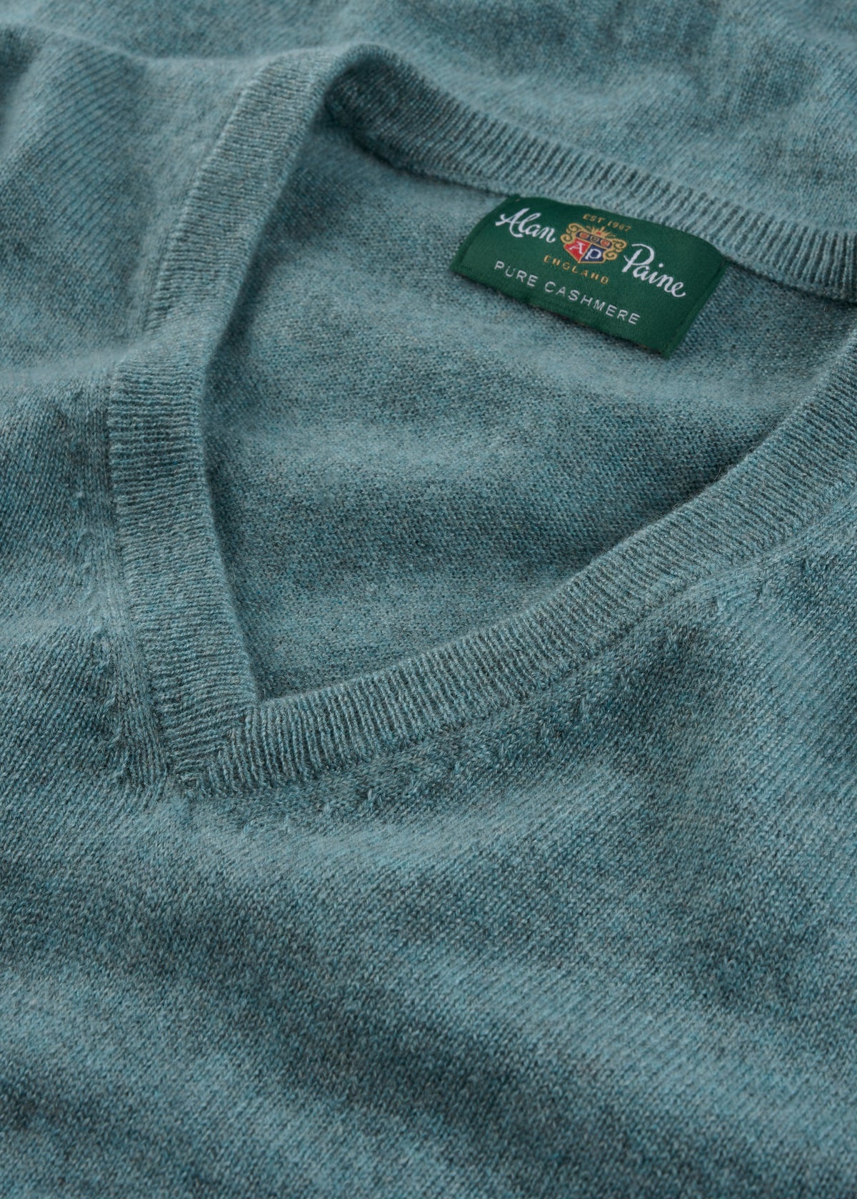 Close-up of the Haddington Pure Cashmere V-Neck Jumper in Caspian with a green Alan Paine label.