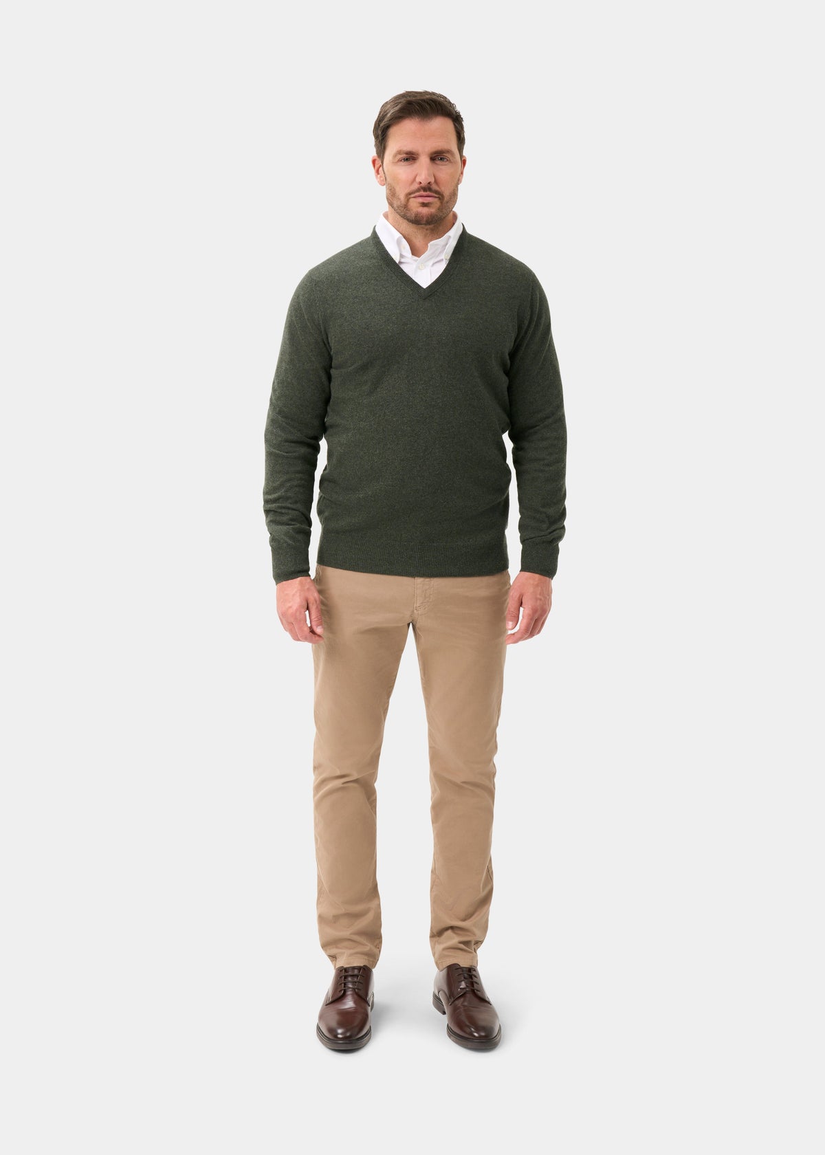 Man in Haddington Pure Cashmere V-Neck Jumper in Rosemary, white shirt, khaki pants, brown shoes on white background.