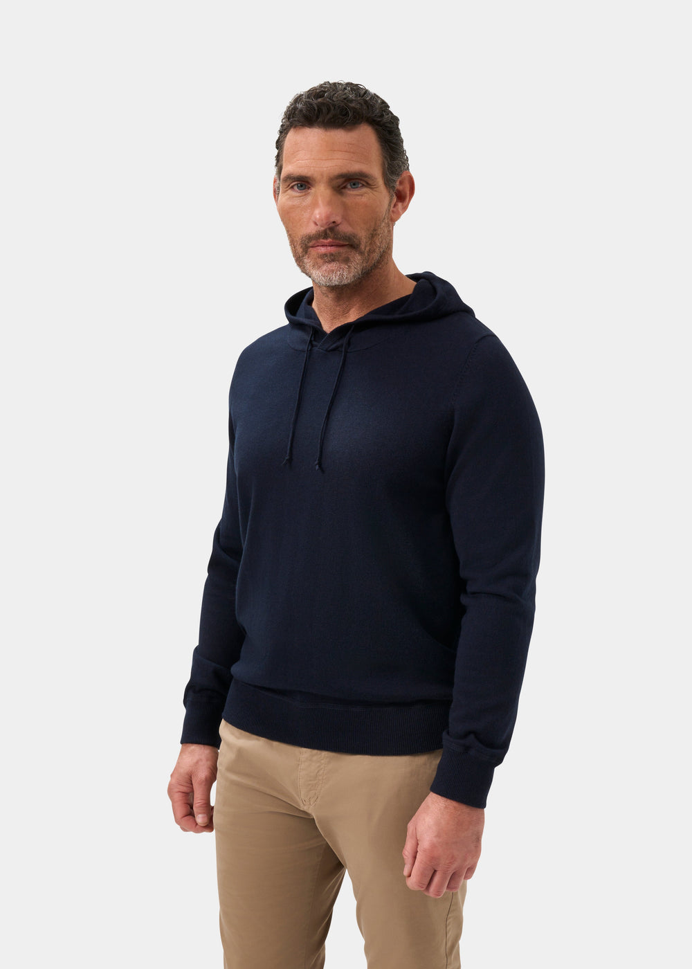 Man wears Gaisby Cotton Merino Hoodie in Dark Navy, regular fit, with beige pants, facing forward on white background.
