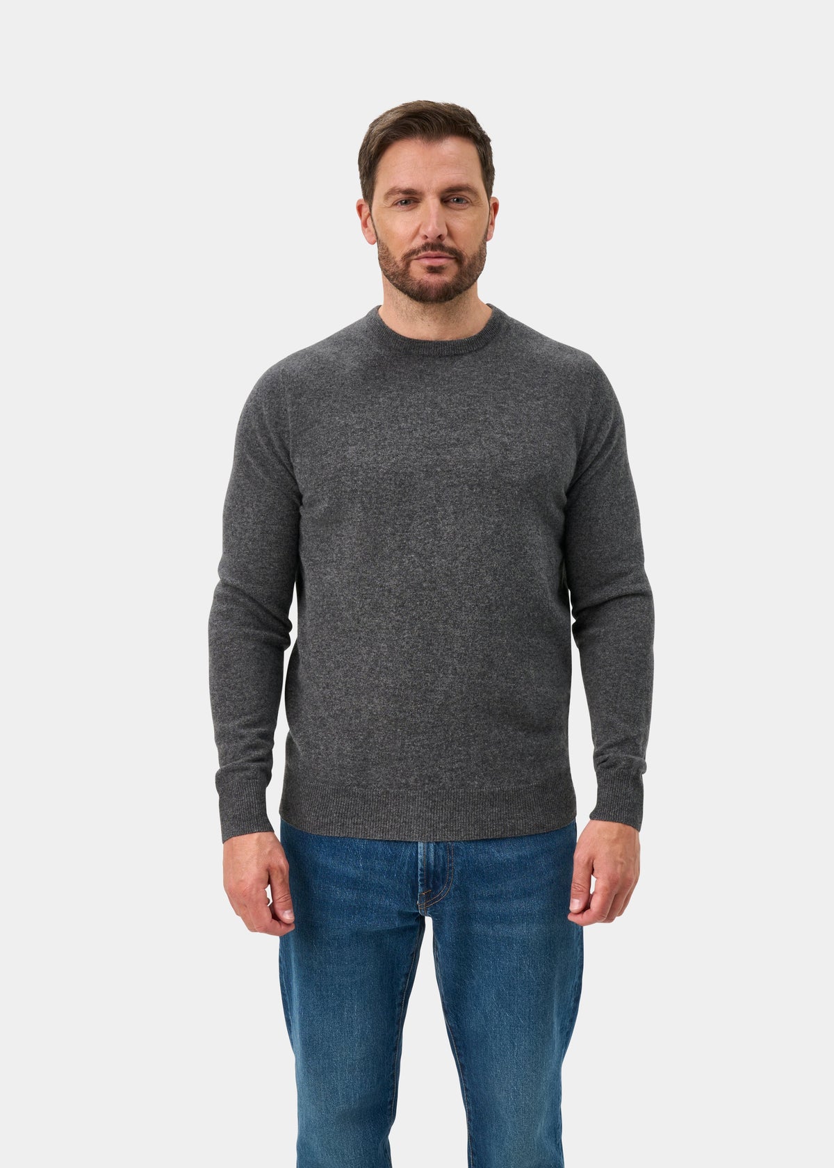 Man wears Brisbane Geelong Wool Crew Neck Jumper in Derby, regular fit, with blue jeans against a white background.