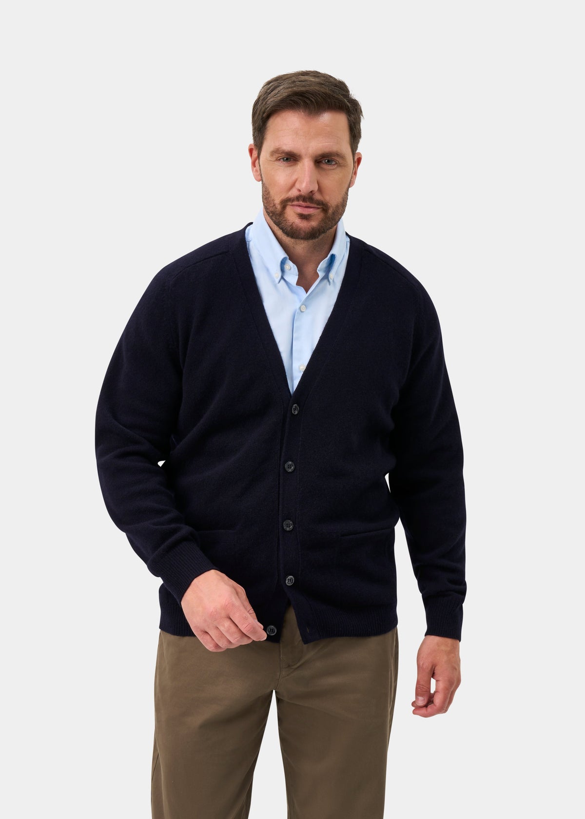Man in Cornwall Lambswool V-Neck Cardigan in Navy, light blue shirt, and khaki pants stands against white background.