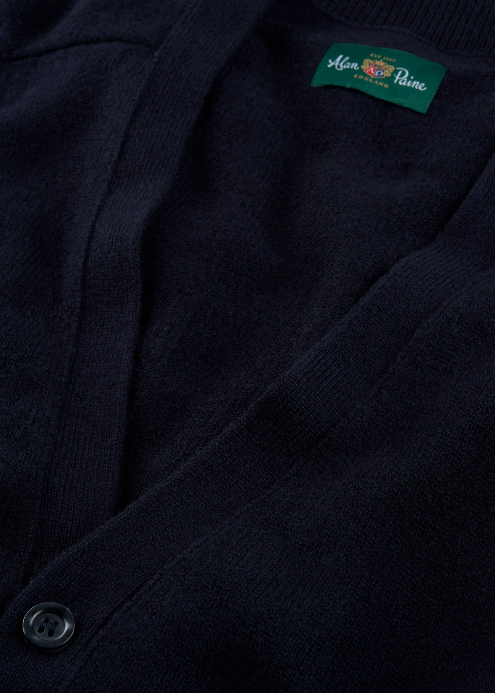 Close-up of the Cornwall Lambswool V-Neck Cardigan in navy, showing a button and green Alan Paine collar label.