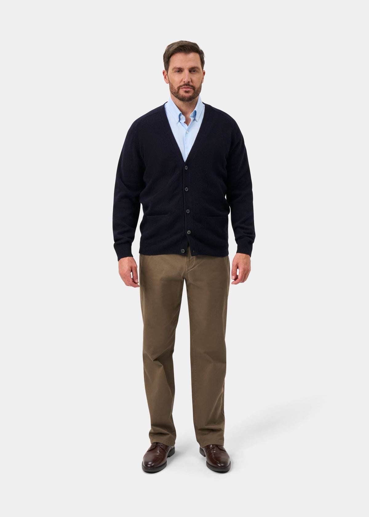 Man in Cornwall Lambswool V-Neck Cardigan in Navy, blue shirt, khaki pants, and brown shoes on white background.