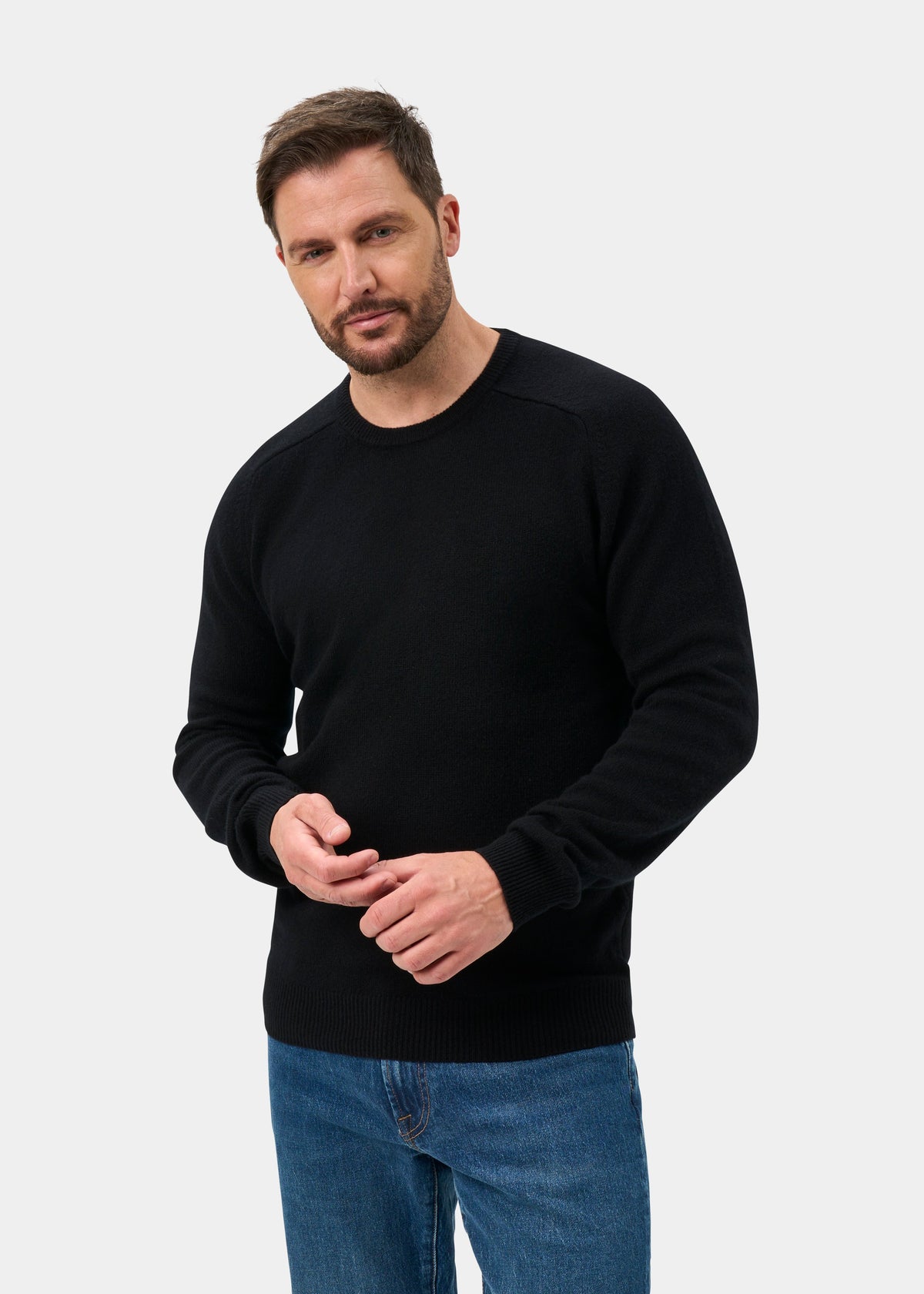Man with short hair sports a Lenzie Lambswool Crew Neck Jumper in black, paired with blue jeans, against a light backdrop.