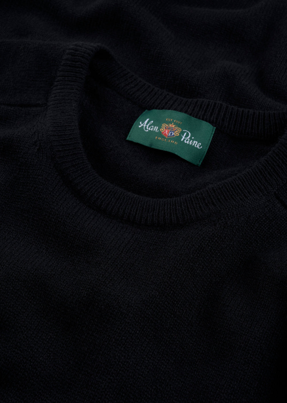 Close-up of Dorset Lambswool Crew Neck Jumper in black, classic fit, with green Alan Paine label inside collar.