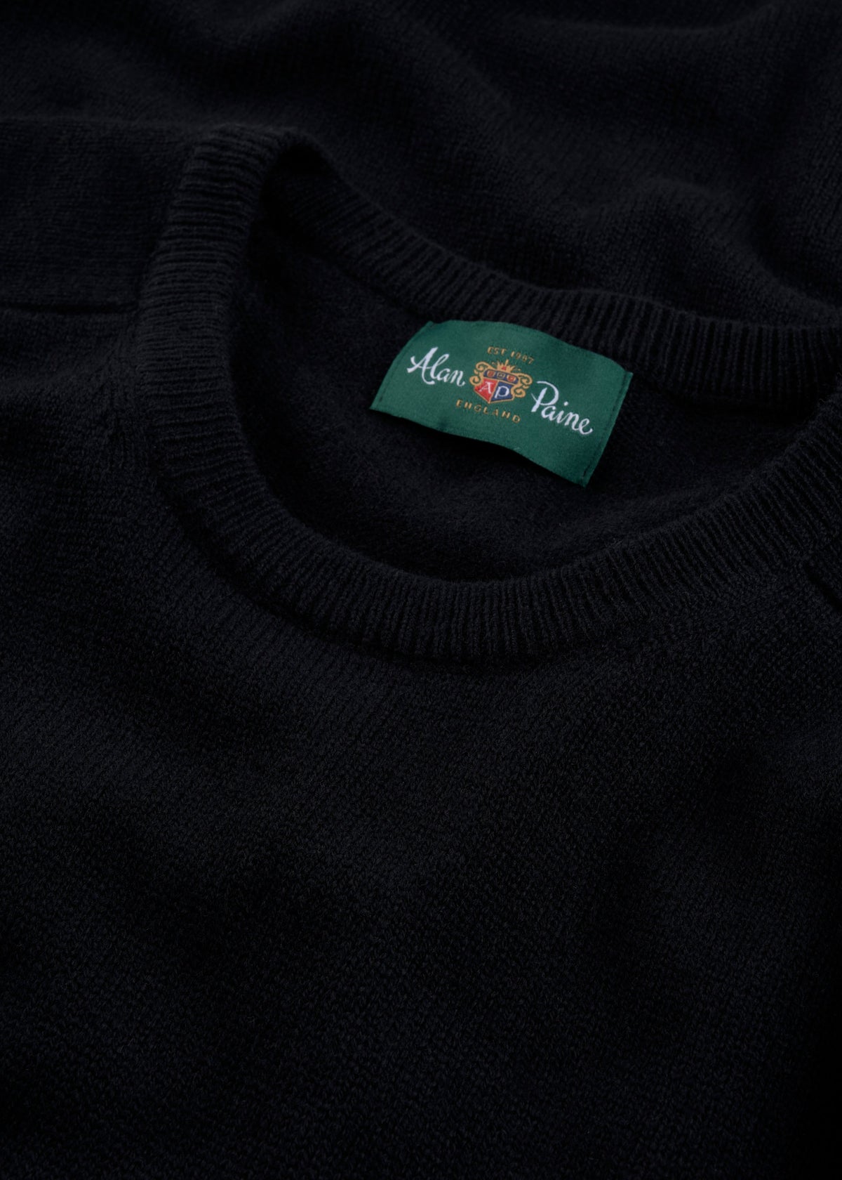 Close-up of Dorset Lambswool Crew Neck Jumper in black, classic fit, with green Alan Paine label inside collar.