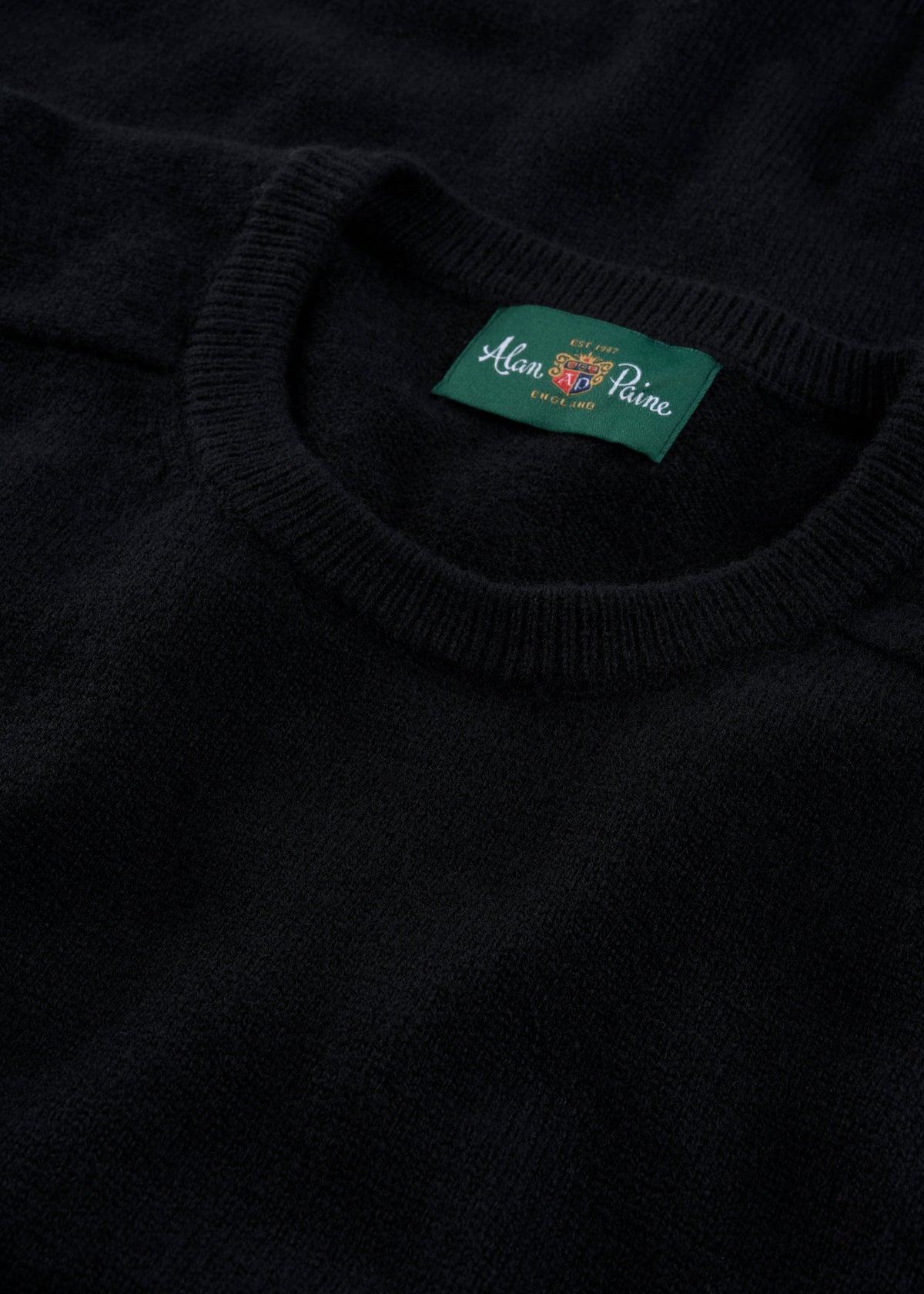 Close-up of Lenzie Lambswool Crew Neck Jumper in black, regular fit, with green Alan Paine label inside the collar.