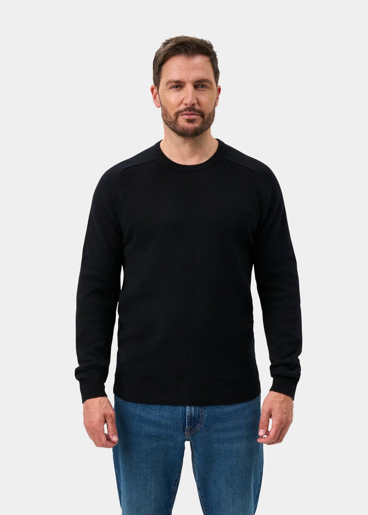 A man with short brown hair models the Lenzie Lambswool Crew Neck Jumper in black, paired with blue jeans.