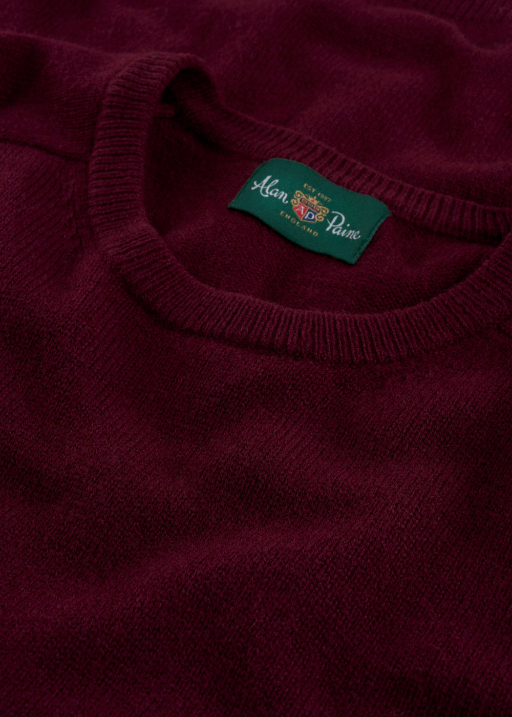 Close-up of the Dorset Lambswool Crew Neck Jumper in Bordeaux, classic fit, with a green Alan Paine collar label.