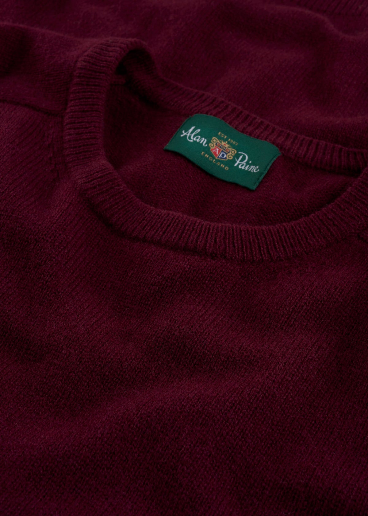 Close-up of the Dorset Lambswool Crew Neck Jumper in Bordeaux, classic fit, with a green Alan Paine collar label.