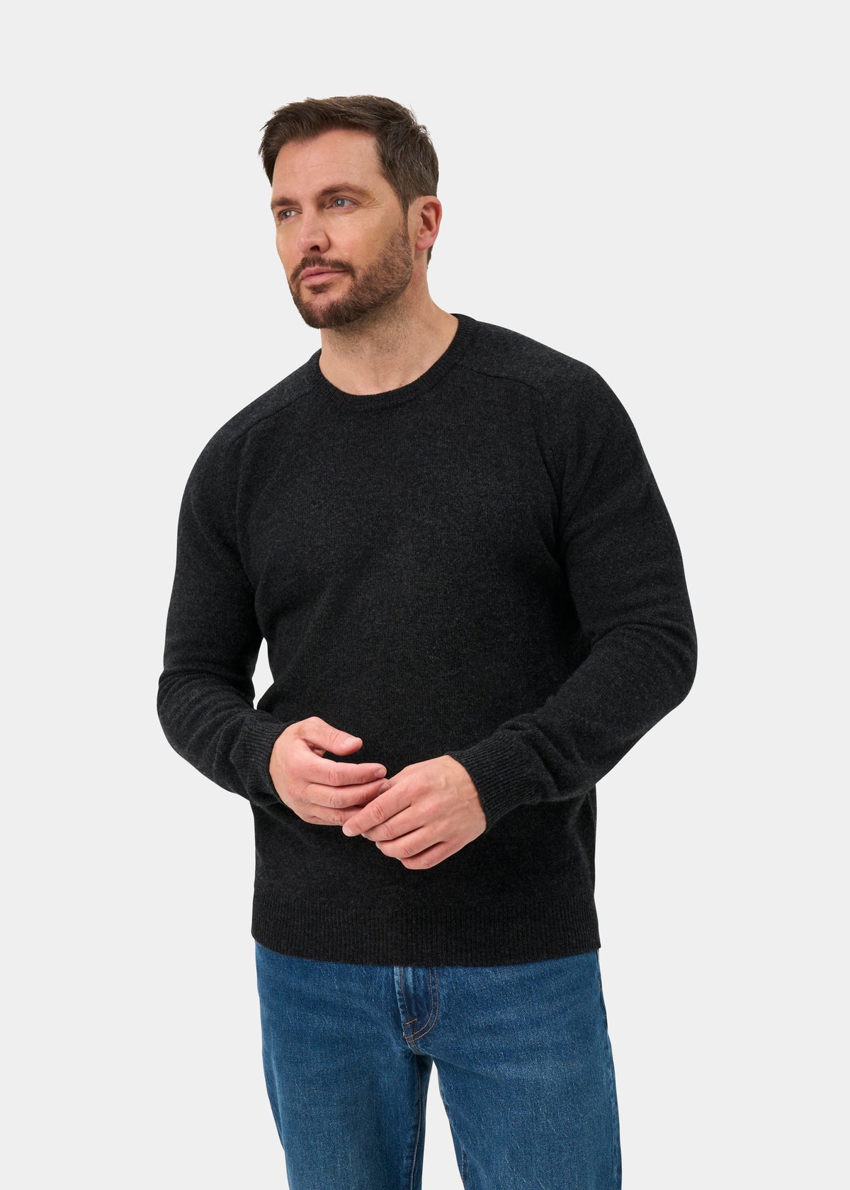 Man with short brown hair wears the Lenzie Lambswool Crew Neck Jumper in Charcoal, paired with blue jeans.