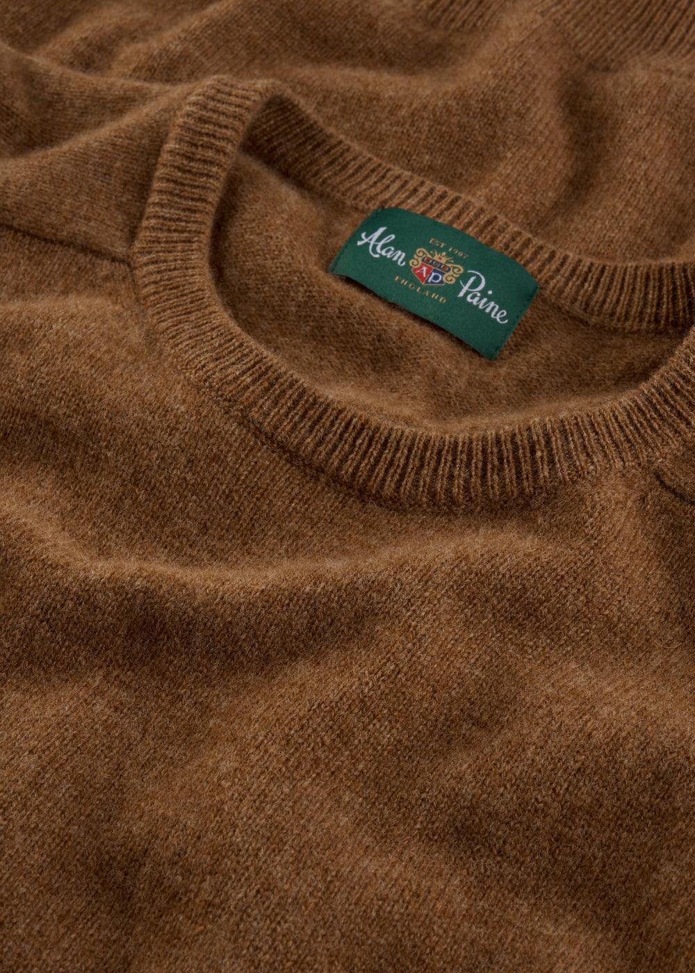 Close-up of the Lenzie Lambswool Crew Neck Jumper in Driftwood, featuring a green Alan Paine England label.
