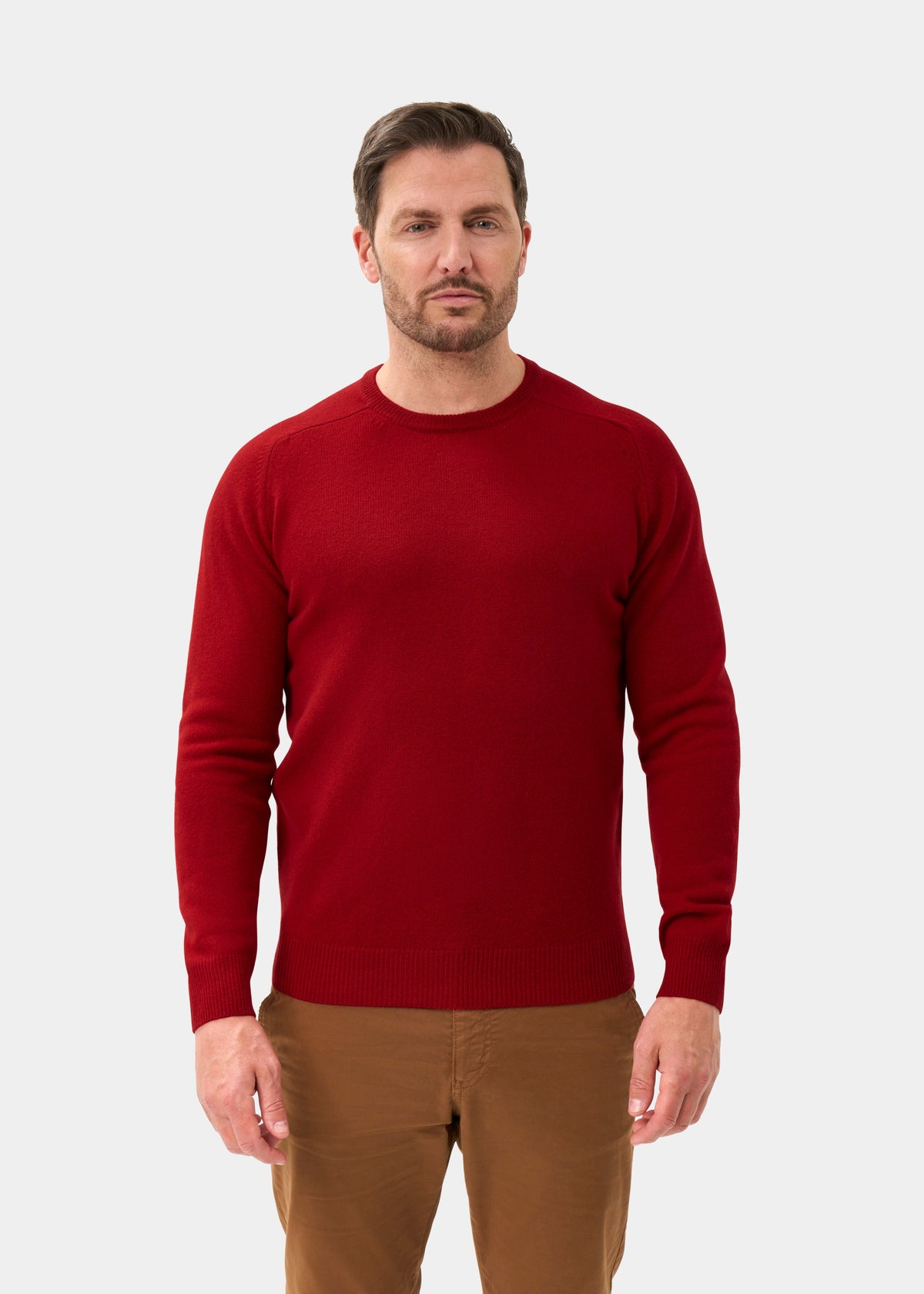 Man in a Lenzie Lambswool Crew Neck Jumper in Dubonnet stands against a plain background, looking at the camera.