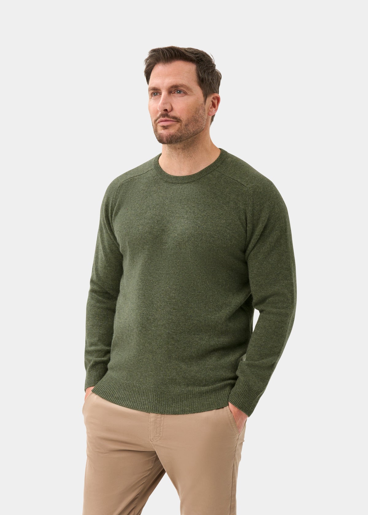 Man in a Lenzie Lambswool Crew Neck Jumper in Landscape and beige pants stands hands-in-pockets against a white background.