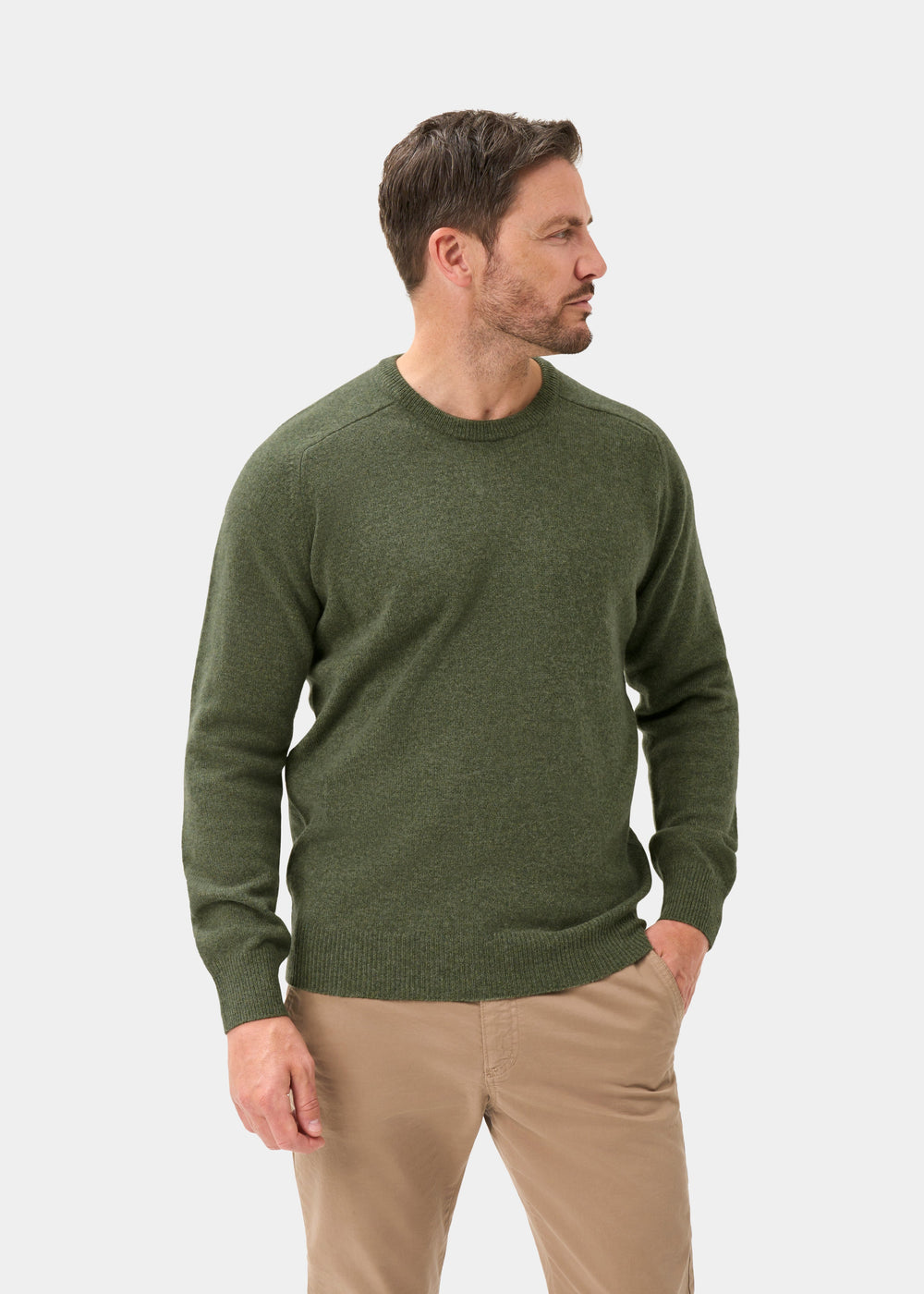 Man wears Dorset Lambswool Crew Neck Jumper In Landscape—Classic Fit, and beige pants, standing with one hand in his pocket.