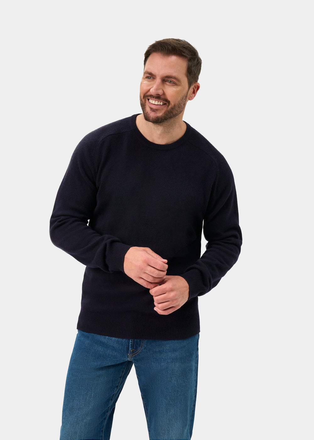 Man in Dorset Lambswool Crew Neck Jumper in Navy smiles, standing against a plain light background.
