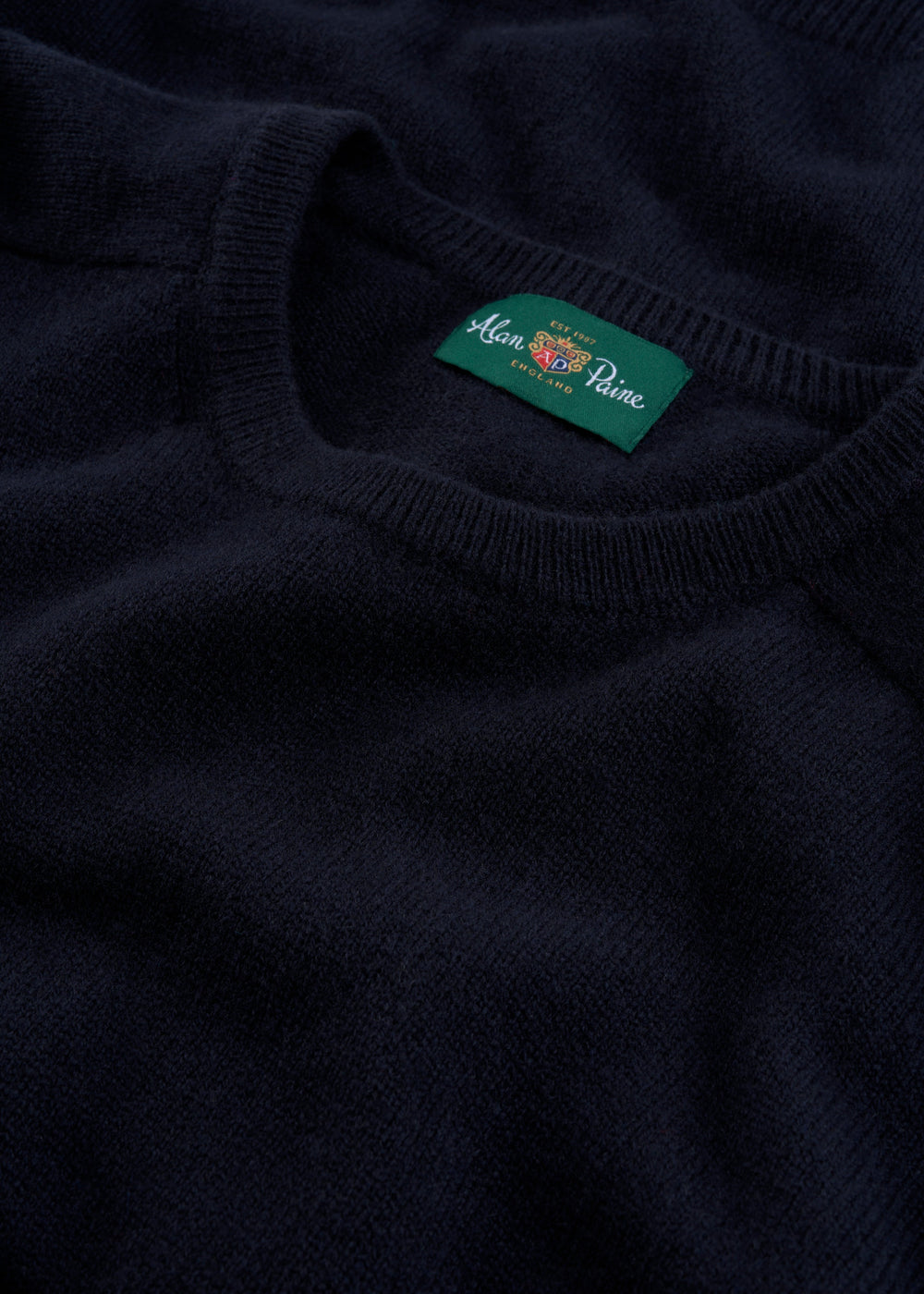 Close-up of the Lenzie Lambswool Crew Neck Jumper in Navy, regular fit, featuring a green brand label at the neck.