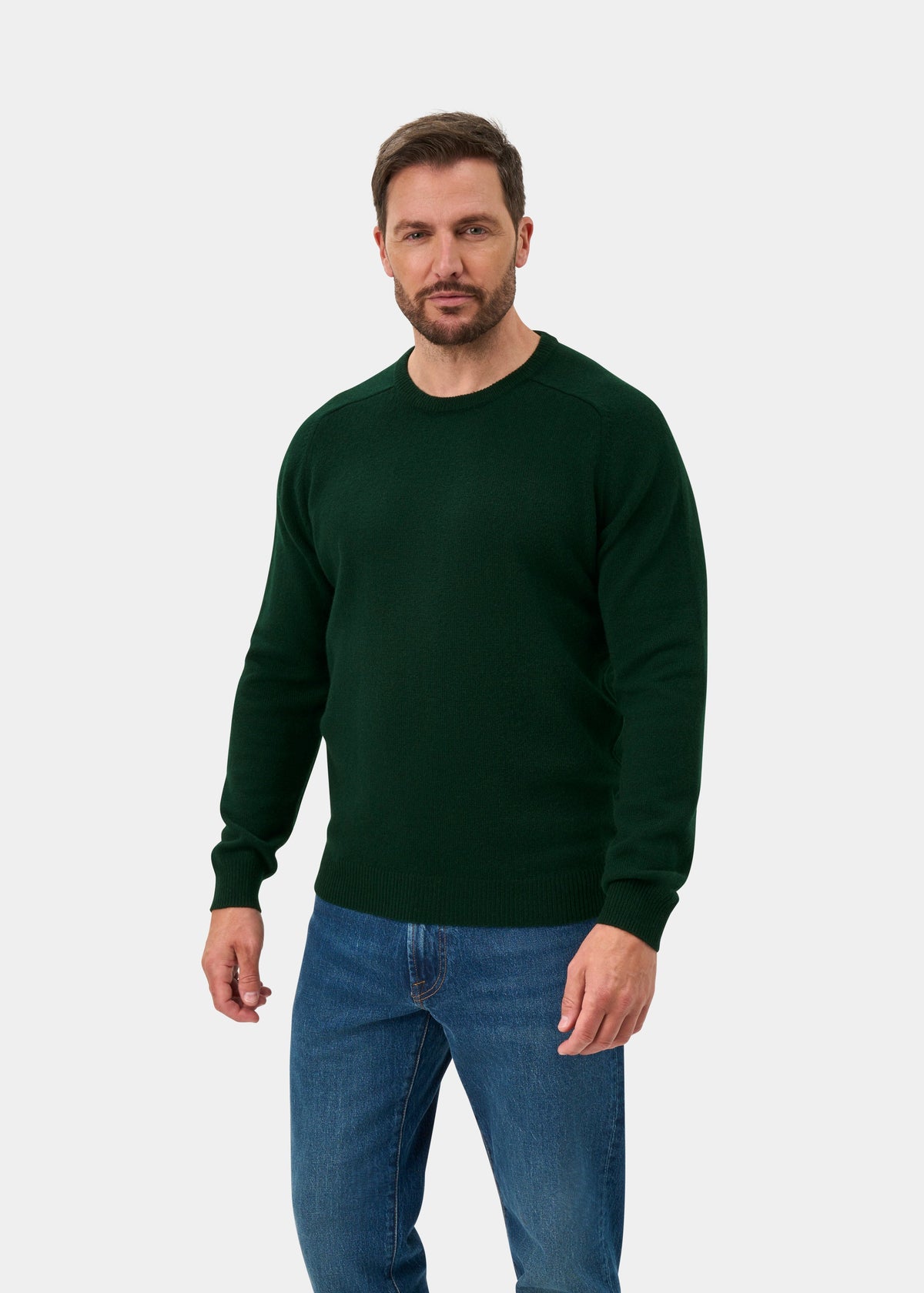 Man in Lenzie Lambswool Crew Neck Jumper in Tartan Green, regular fit, and blue jeans against a light background.