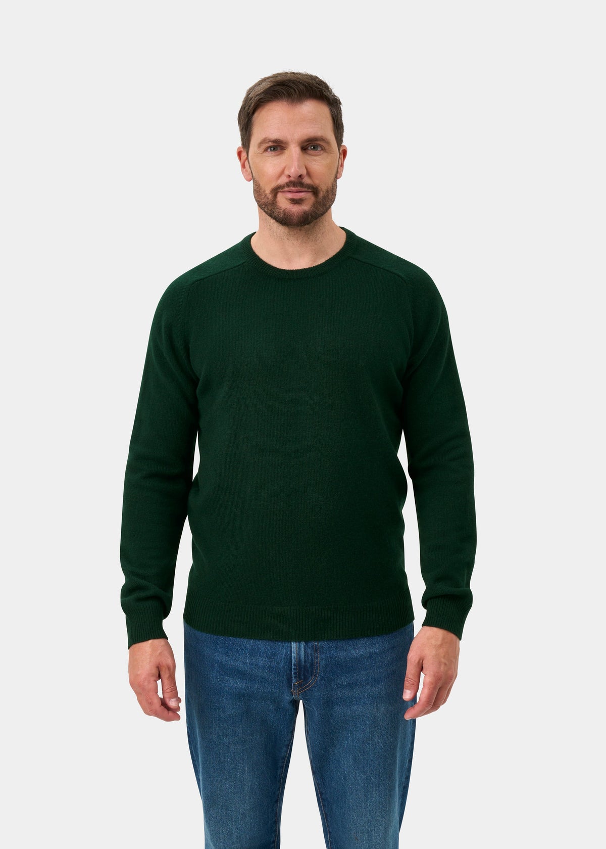 Man wears Lenzie Lambswool Crew Neck Jumper in Tartan Green and blue jeans, facing forward on a white background.