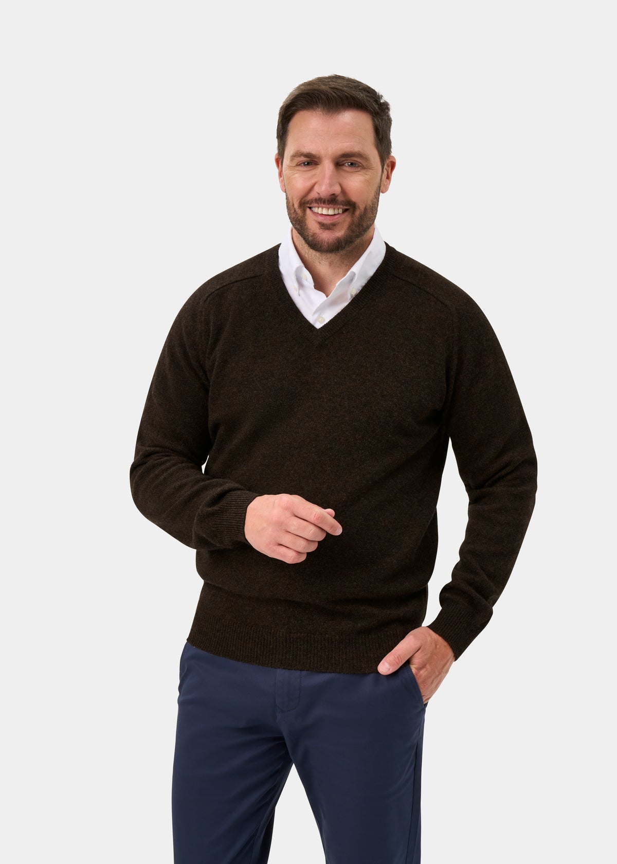 Man in a Kilsyth Lambswool Vee Neck Jumper in Cocoa smiles, standing against a plain white background.