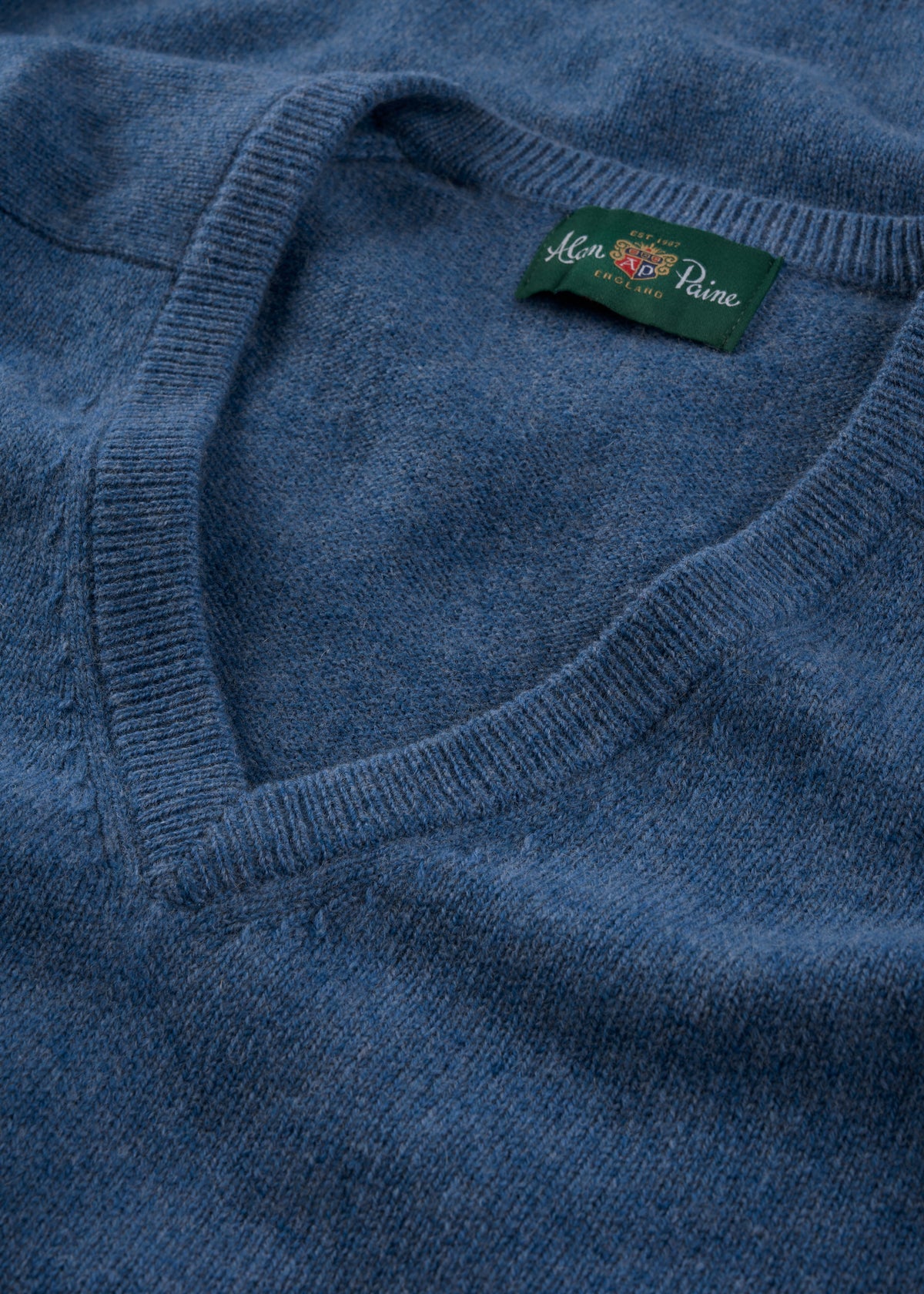 Close-up of the Hampshire Lambswool Vee Neck Jumper in Jeans with a green label near the collar.