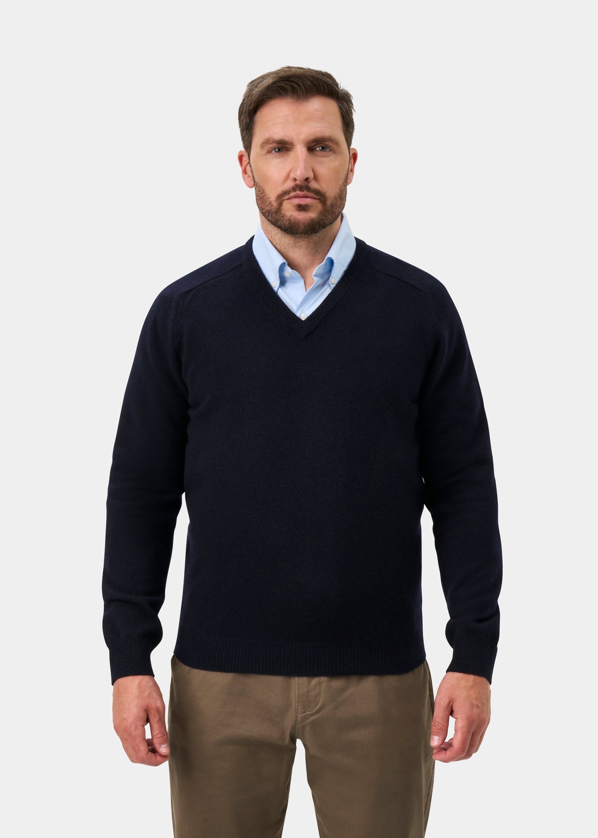 Man in Kilsyth Lambswool V-Neck Jumper in Navy, light blue shirt, and khaki pants against a plain background.