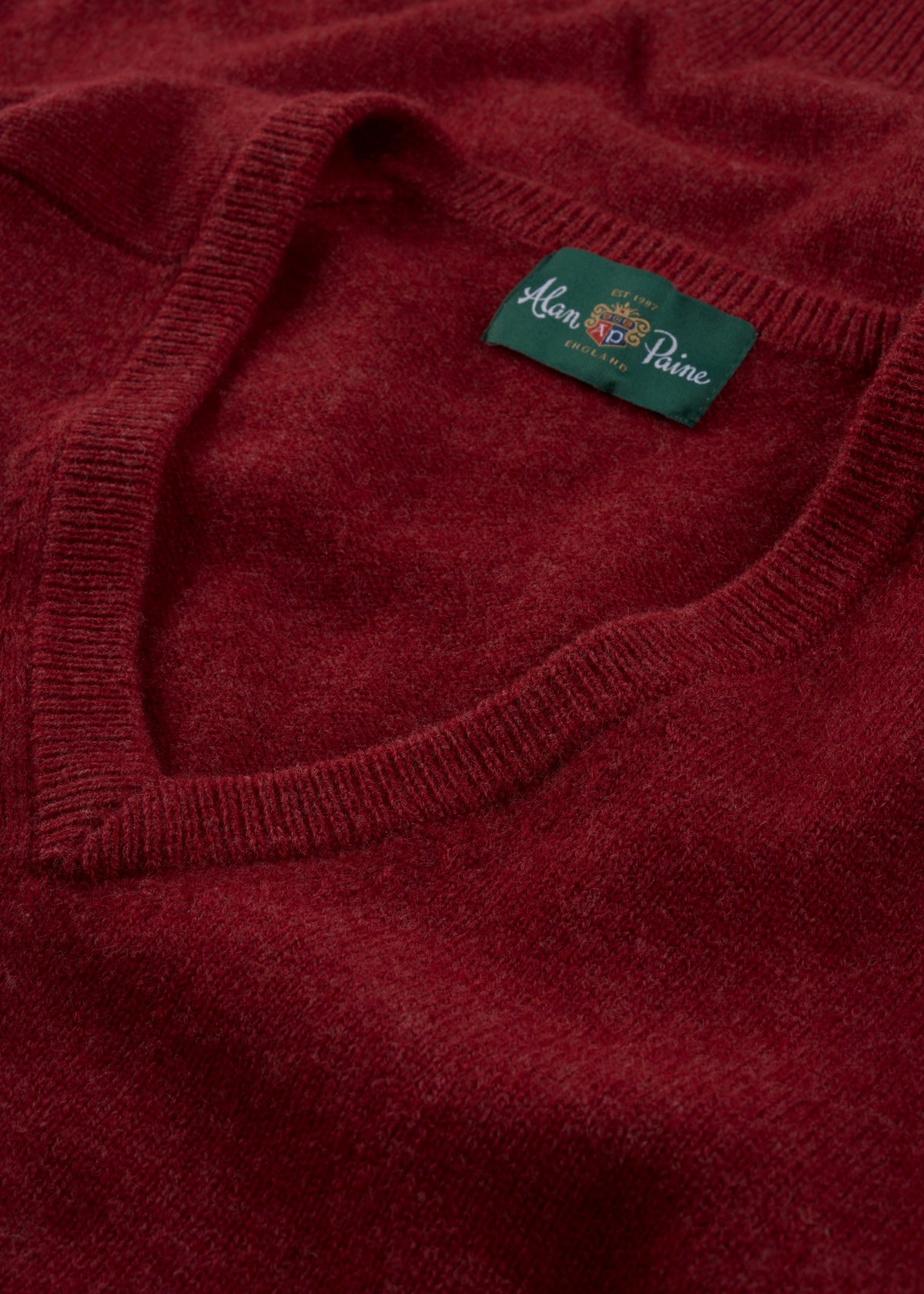 Close-up of a red Hampshire Lambswool Vee Neck Jumper in Poppy, classic fit, with green Alan Paine label at collar.
