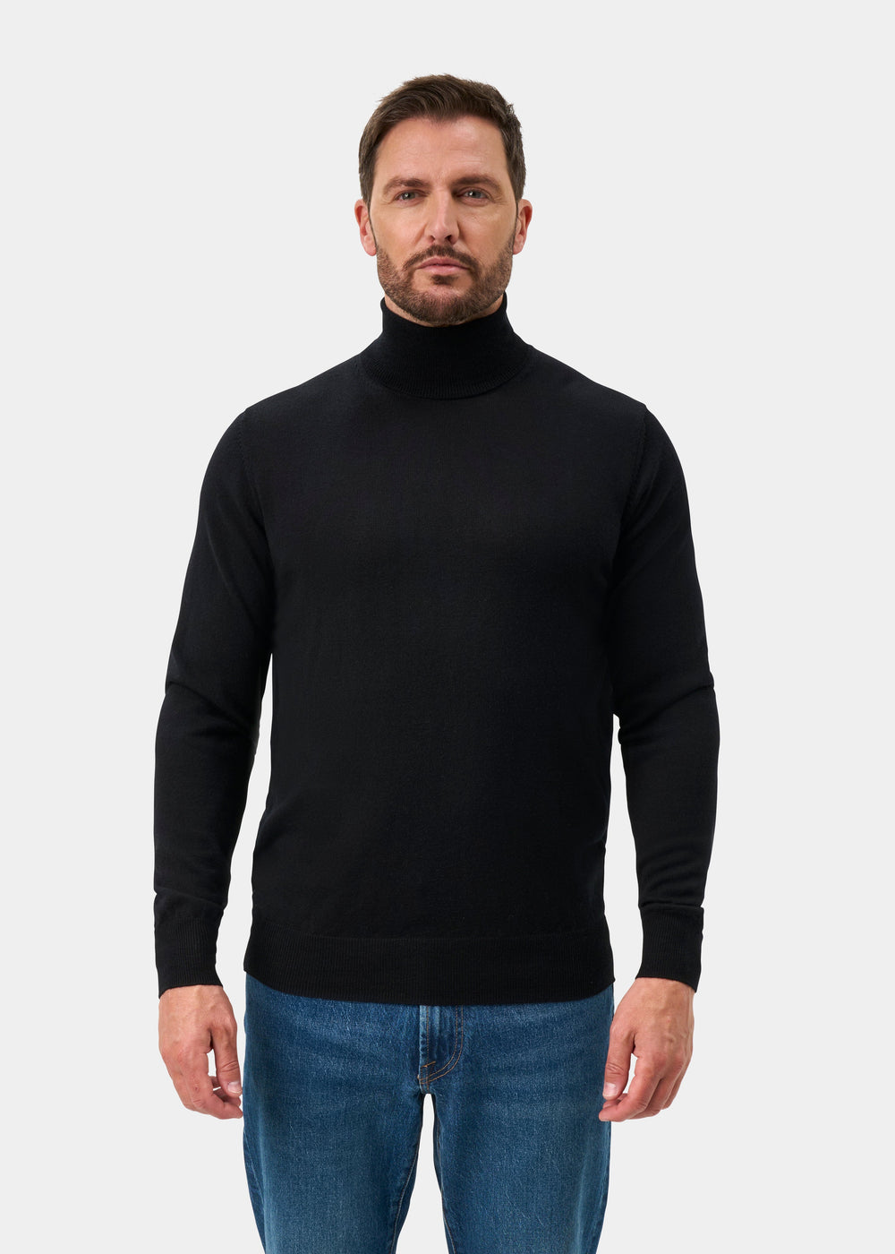 Man in Linton Merino Wool Roll Neck Jumper in Black, Regular Fit, and blue jeans stands against a white background.