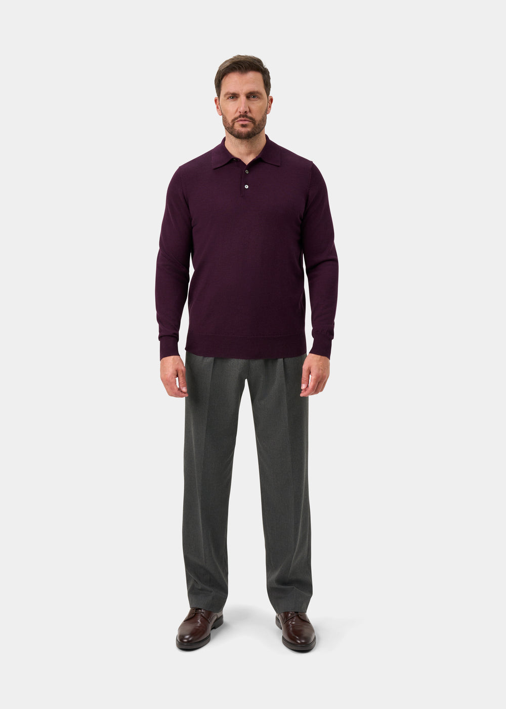 Man wearing Hindhead Men’s Merino Wool Polo Shirt in Black Grape, gray trousers, brown shoes, on a white background.