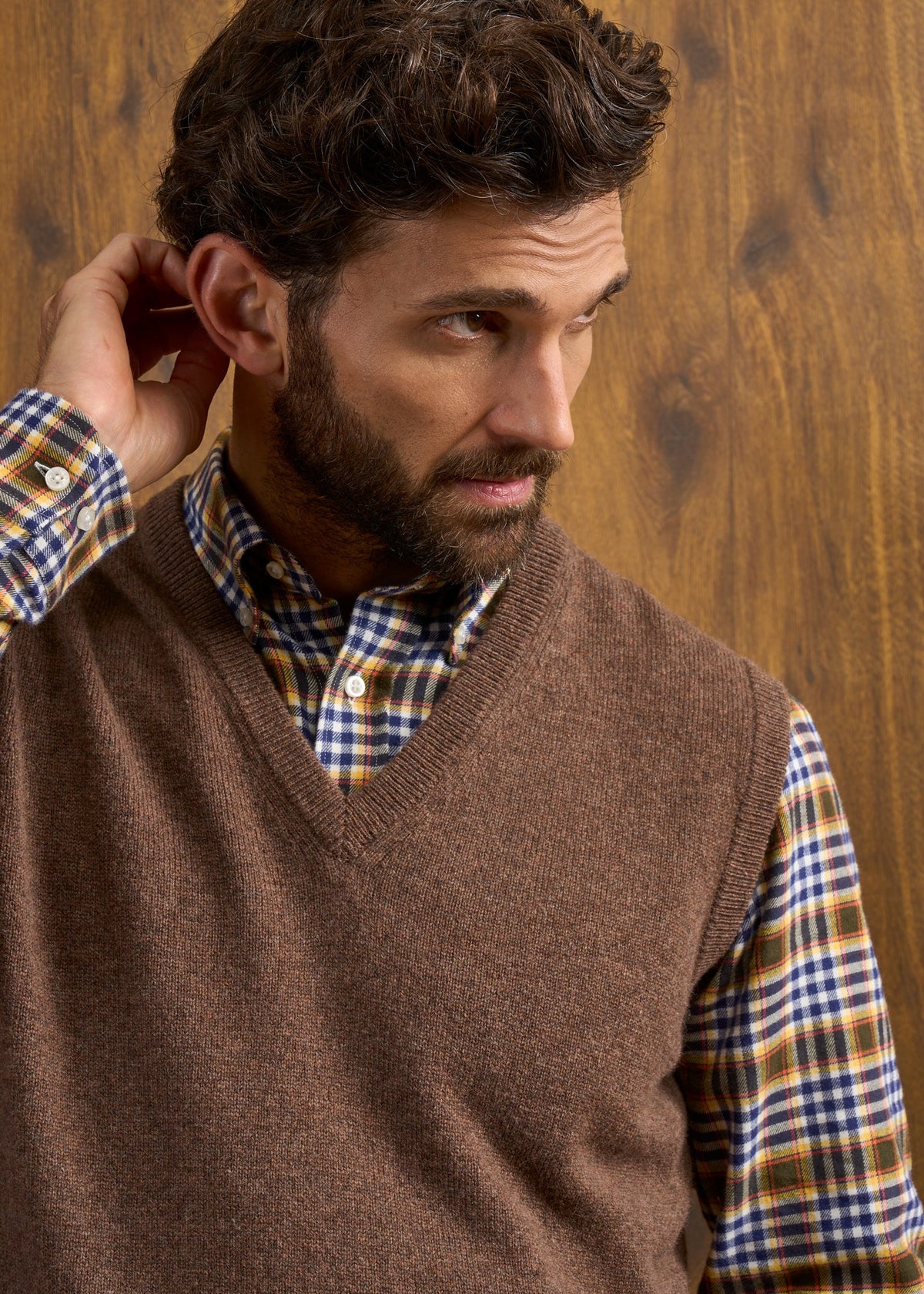 A man wearing a Norfolk Lambswool V-Neck Slipover In Tobacco over a colorful plaid shirt.