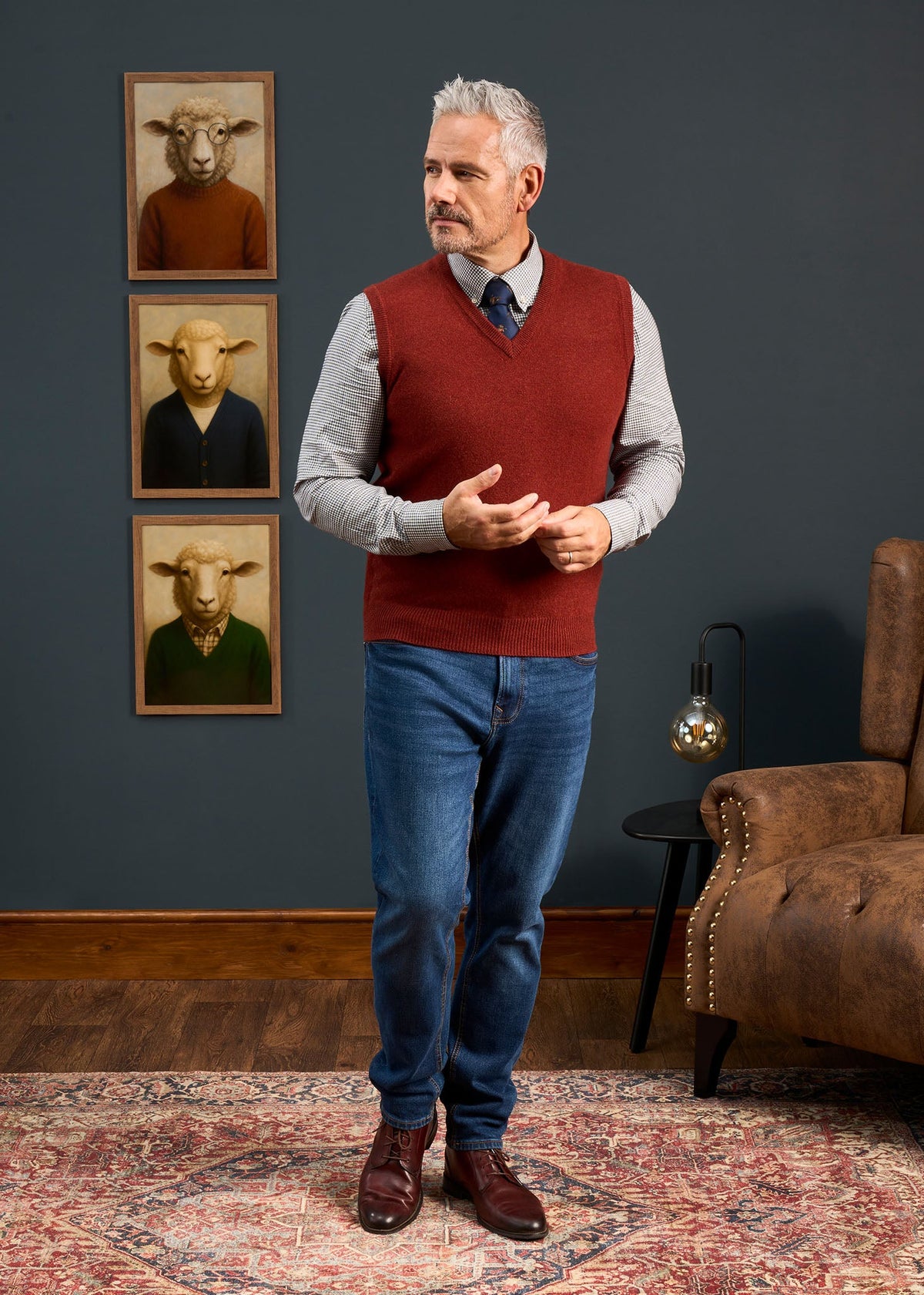 A man in a Norfolk Lambswool V-Neck Slipover In Sienna, worn over a patterned button-down shirt and blue jeans.