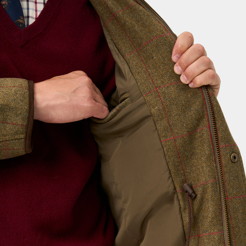 Close-up of a person wearing a brown tweed zip-front jacket with a red windowpane check pattern, opening it to reveal a padded olive-brown lining. The person is also wearing a burgundy sweater.