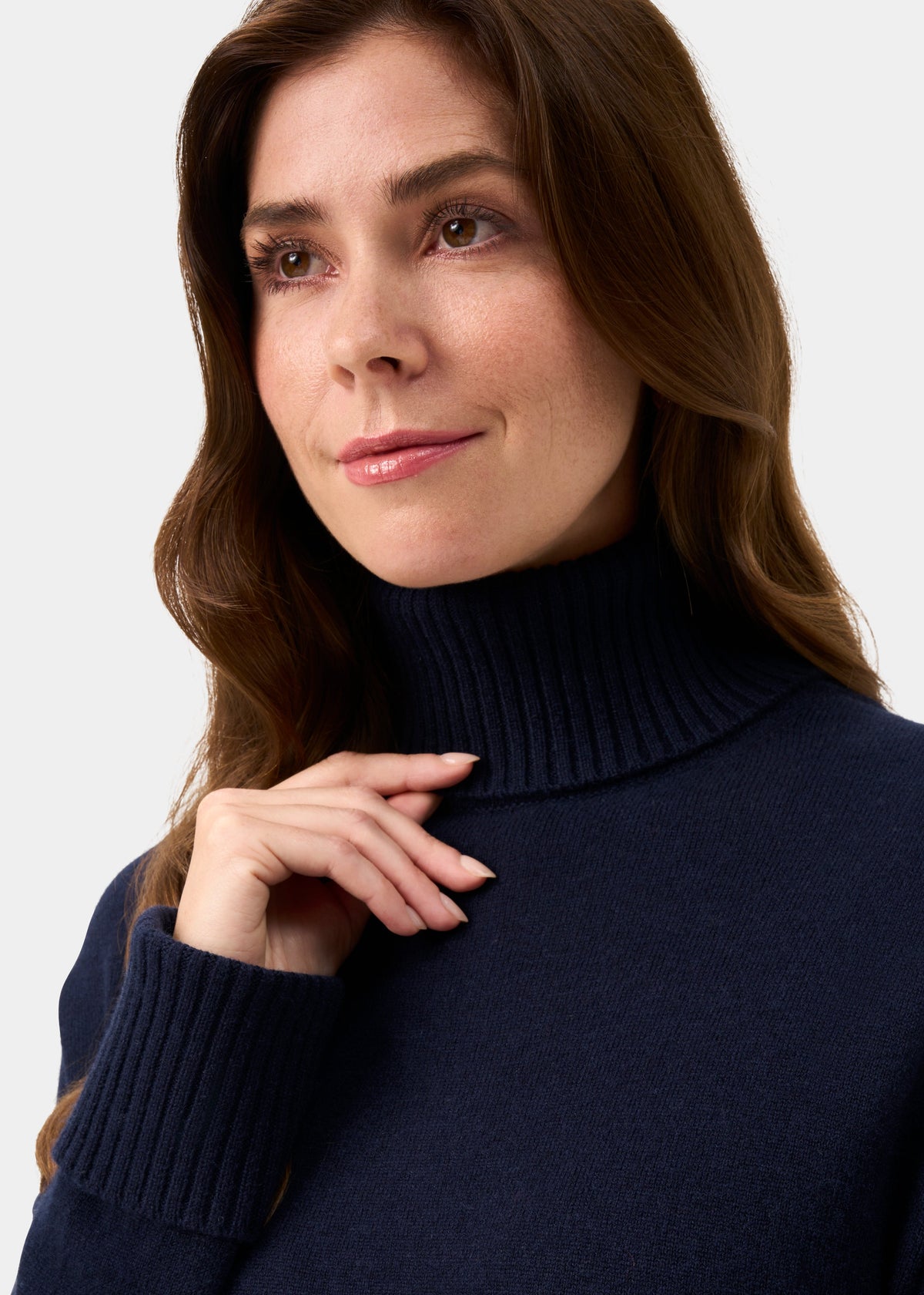 Woman in Alexa Wool & Cashmere Roll Neck Jumper in dark navy, looks up, smiling softly, hand on collar.