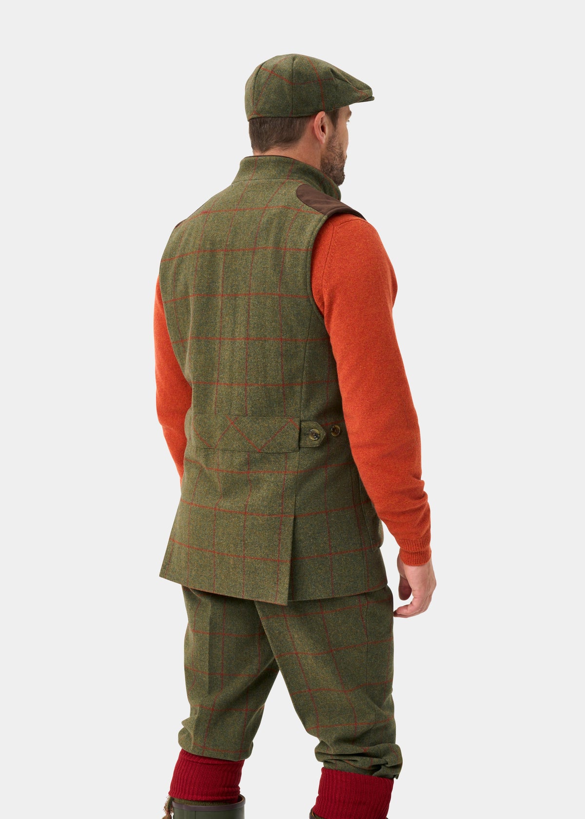 Man in Combrook Men’s Tweed Water Repellent Shooting Gilet in Reed, matching pants, orange sweater, cap, red socks.