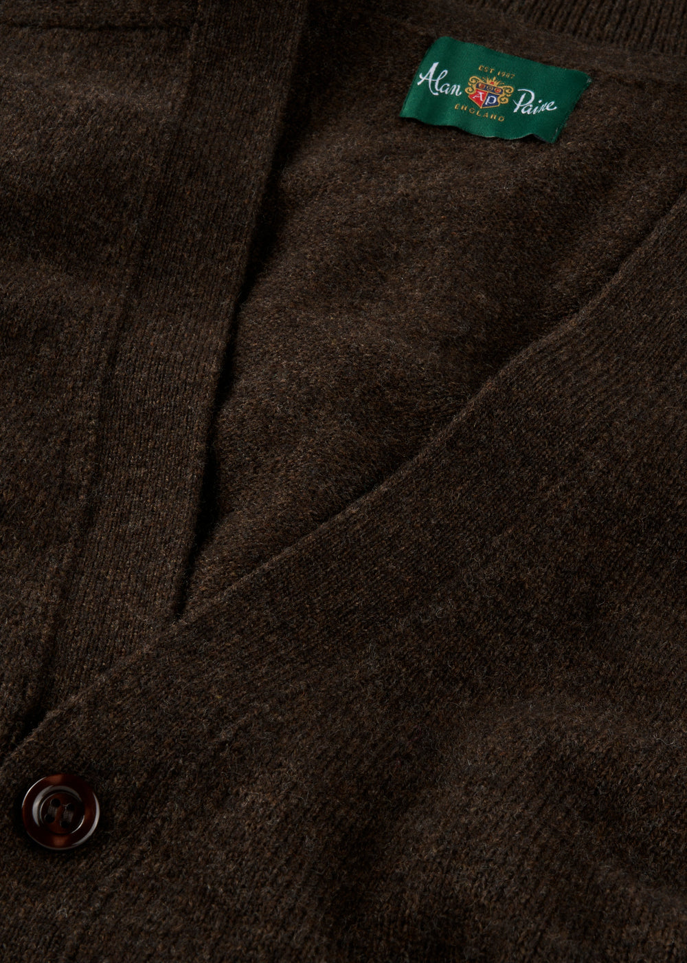 Close-up of Cornwall Lambswool V-Neck Cardigan in Cocoa, classic fit, with a button and green Alan Paine label.