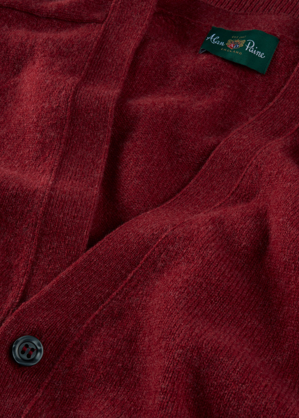 Close-up of the Cornwall Lambswool V-Neck Cardigan in Poppy Melange with black button and green collar label.
