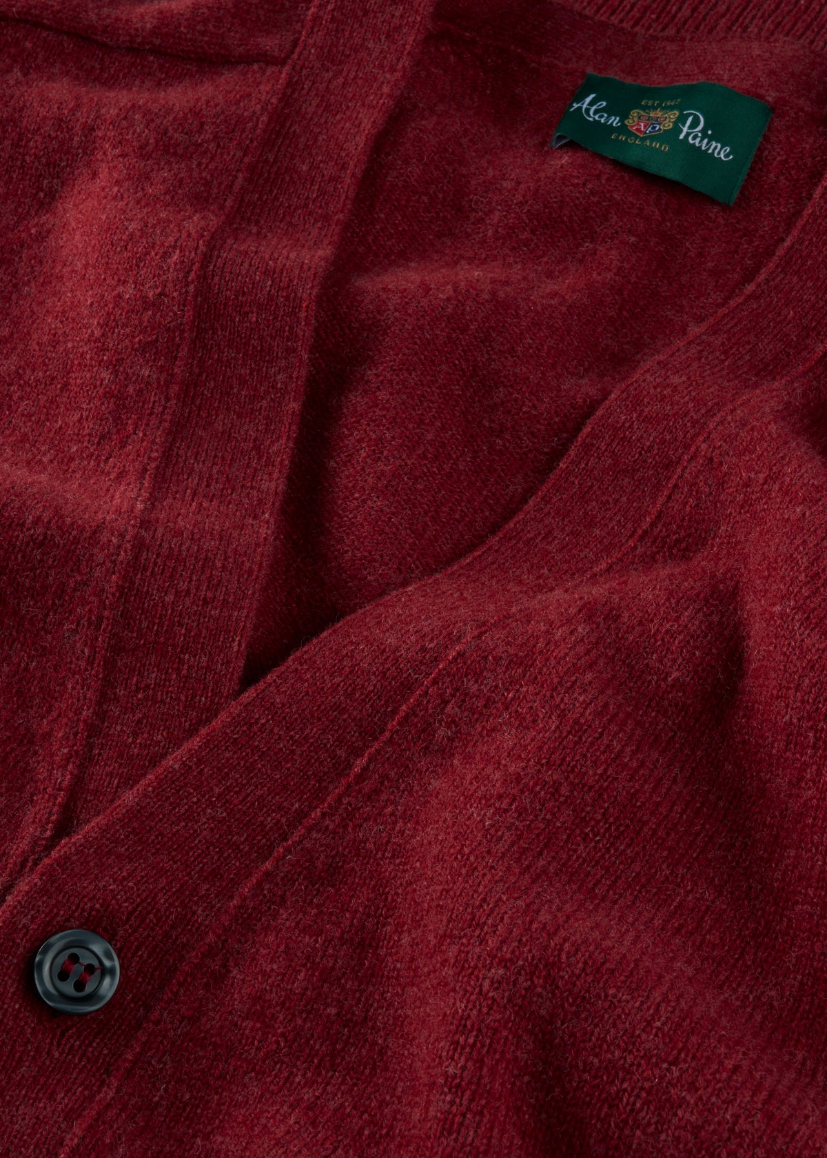 Close-up of the Cornwall Lambswool V-Neck Cardigan in Poppy Melange with black button and green collar label.