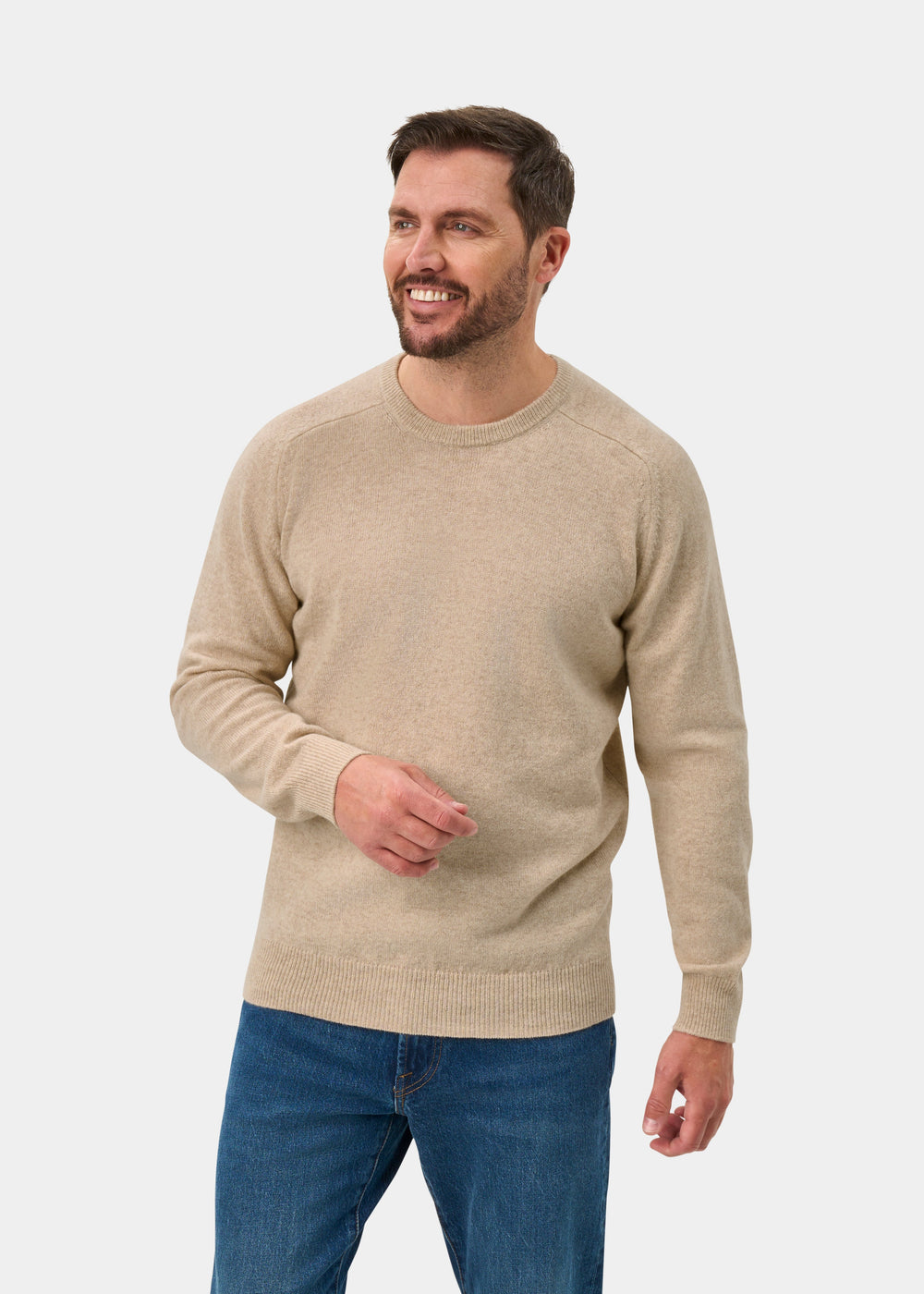 Man in Dorset Lambswool Crew Neck Jumper in Linen, classic fit, and blue jeans smiles against a plain white background.
