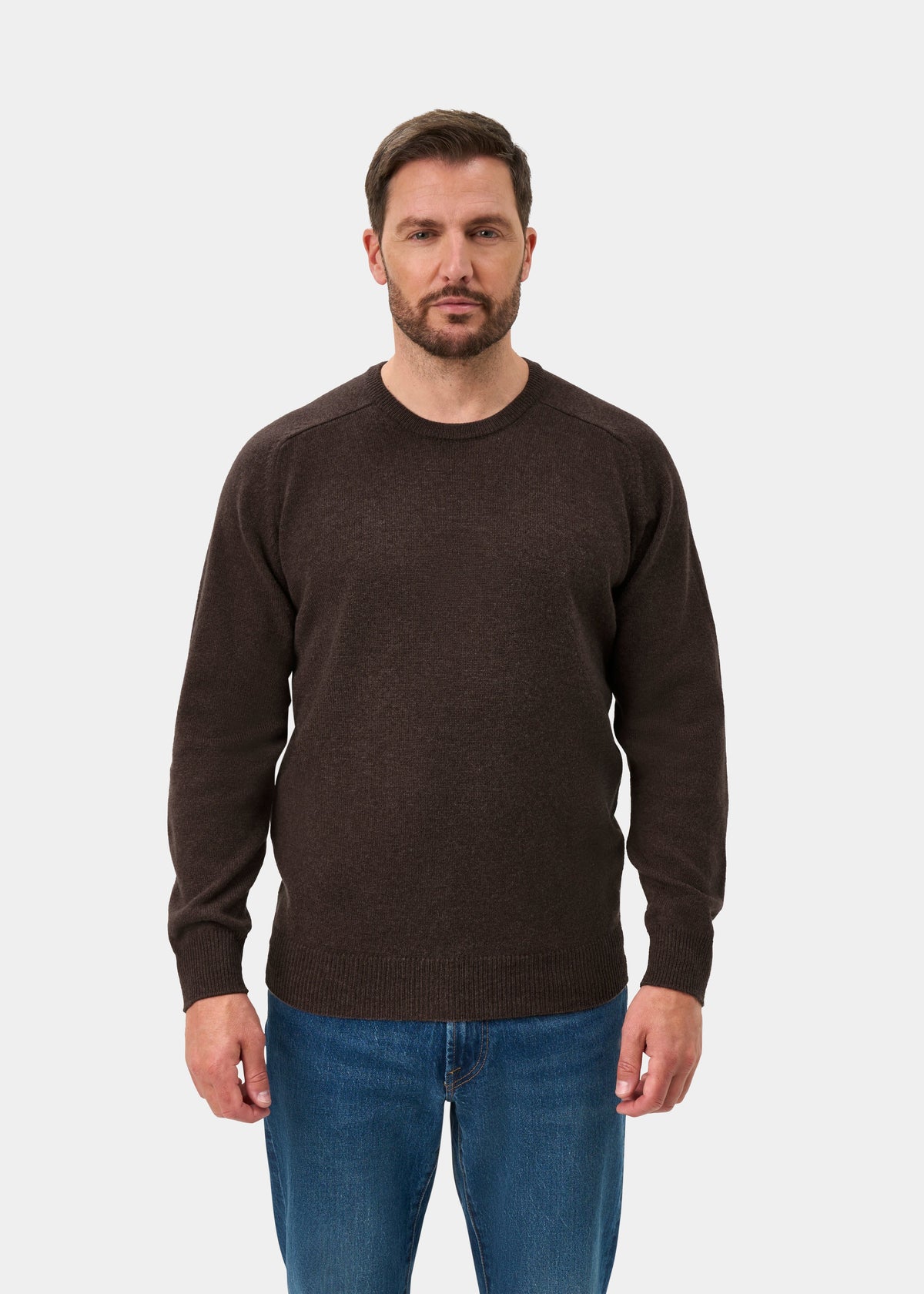 Man in Dorset Lambswool Crew Neck Jumper in Mocha, classic fit, and blue jeans channels countryside style.