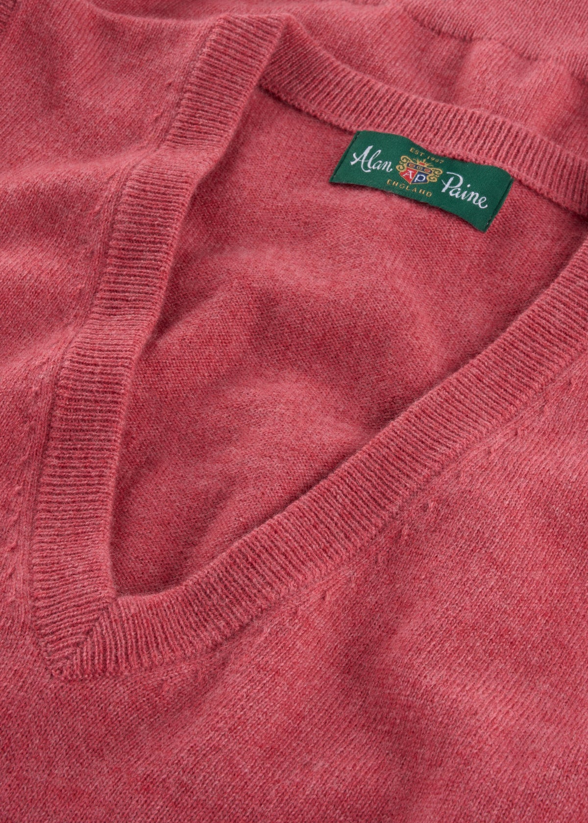 A close-up of an Erin Wool & Cashmere V-Neck Slipover in Rouge with a green Alan Paine England label.