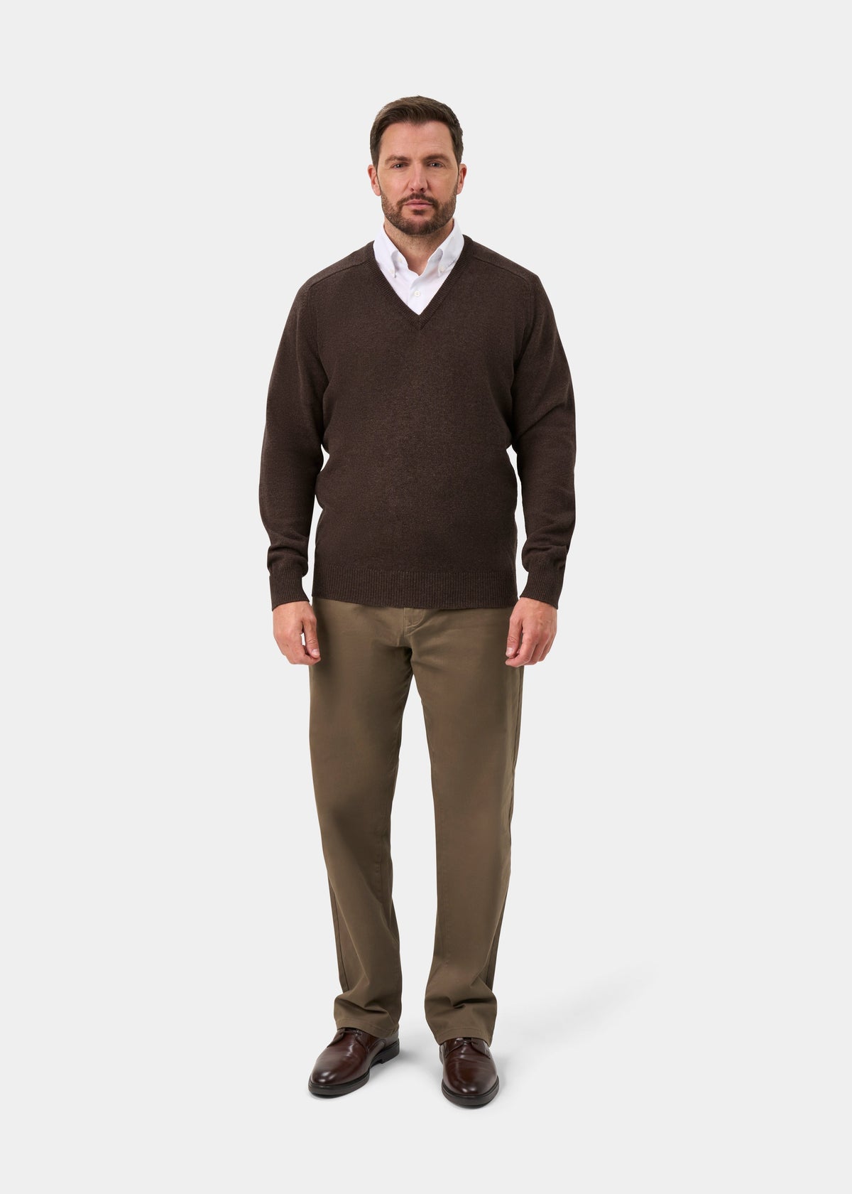 Man in a Hampshire Lambswool V-Neck Jumper in Mocha, white shirt, tan pants, and brown shoes on a plain background.