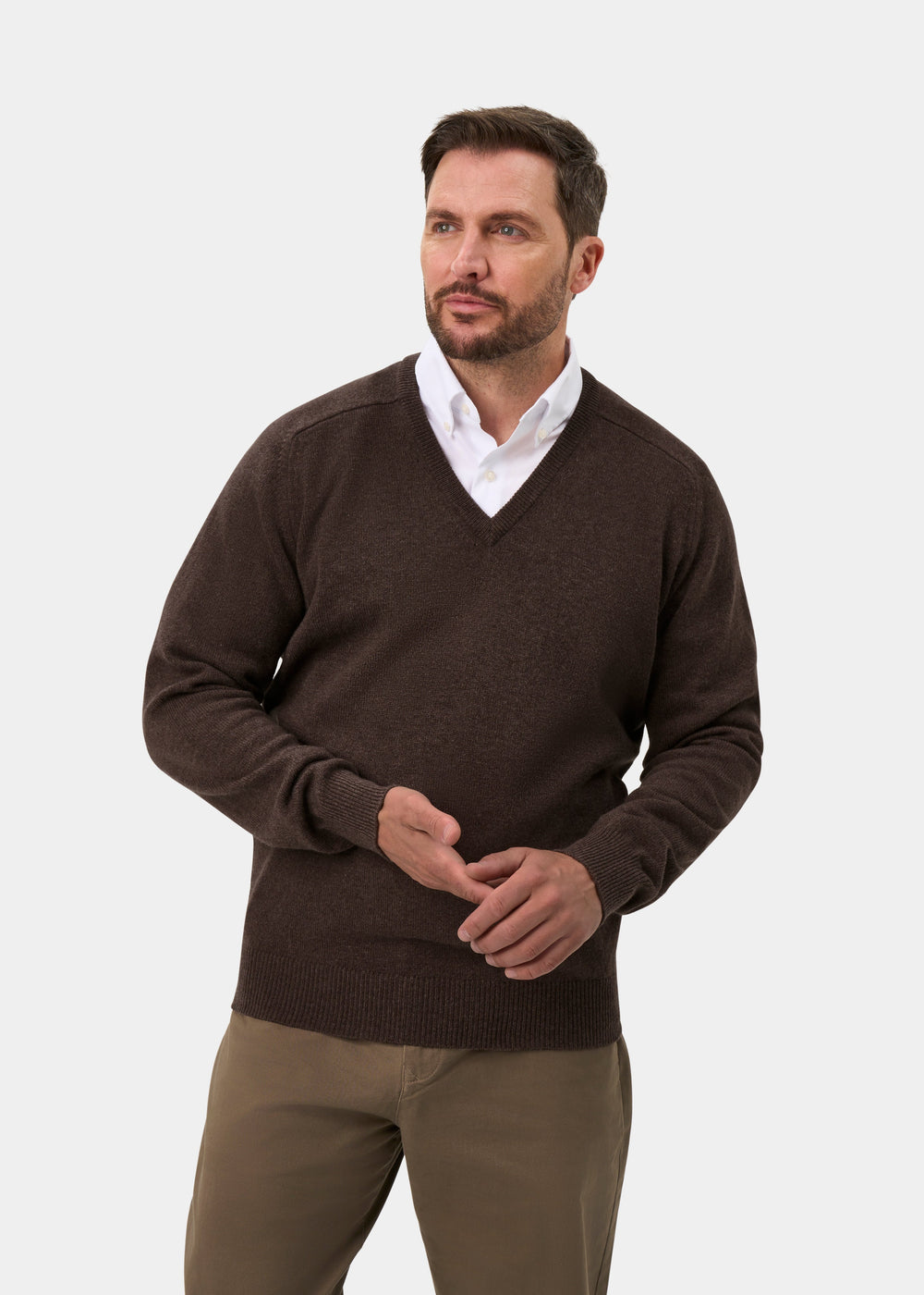 Man wears the Hampshire Lambswool V-Neck Jumper in Mocha—classic fit—paired with khaki pants, gazing to the side.