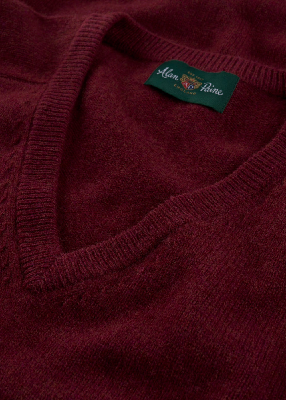 Close-up of Kilsyth Lambswool V-Neck Jumper in Garnet, Regular Fit, featuring green Alan Paine label.